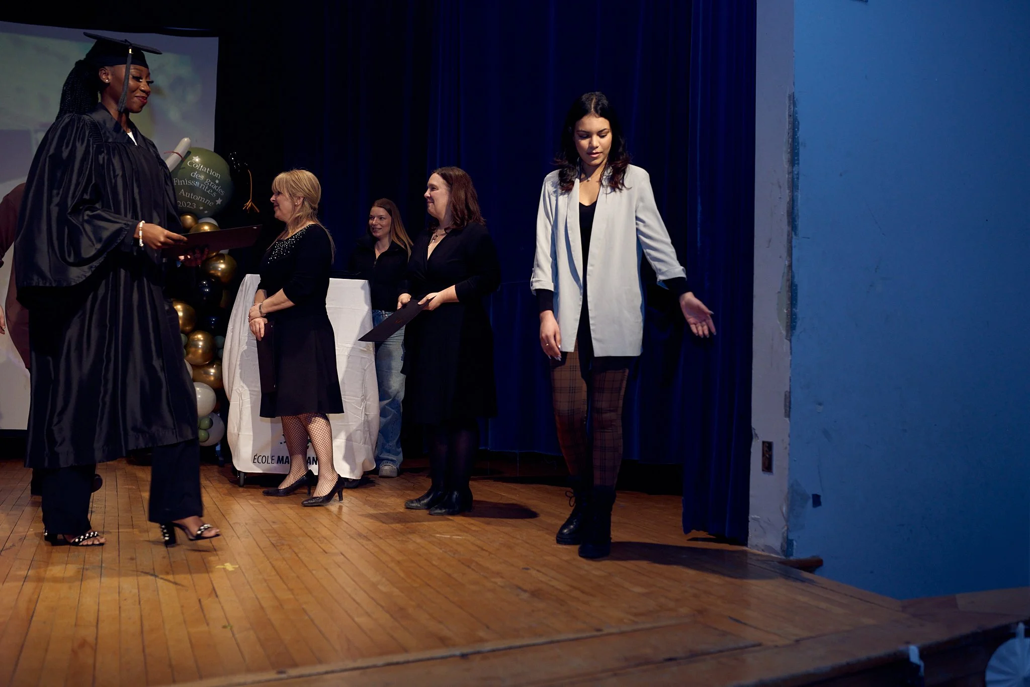 Une cérémonie de remise de diplômes avec des étudiants en robe de gradué sur une scène, recevant leurs diplômes et félicitations.