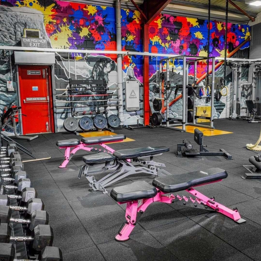 Interior of a gym with colorful wall art, featuring weights, benches, and exercise equipment.