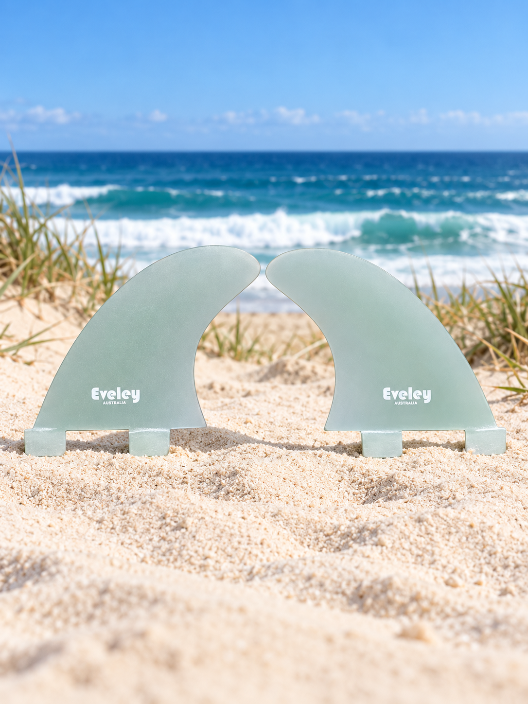 Two Eveley 3.6-inch natural Pro Glass side fins standing on an Australian sand dune with a surf beach behind.