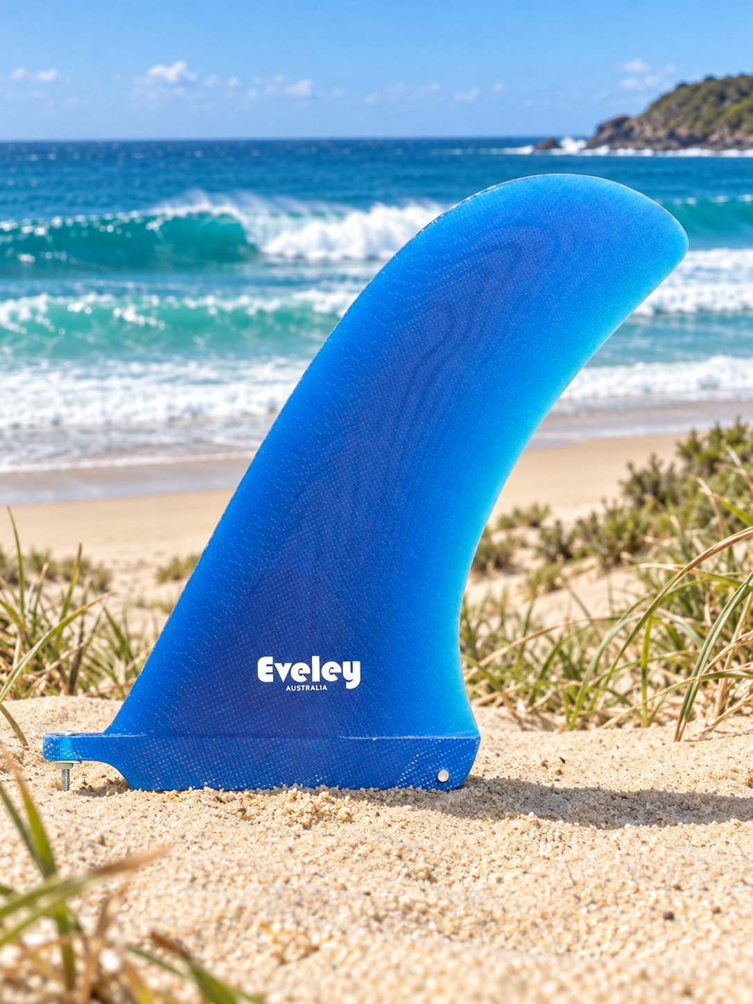 Blue Santa Monica fin standing in dune sand with breaking surf behind and the Eveley Australia logo visible.