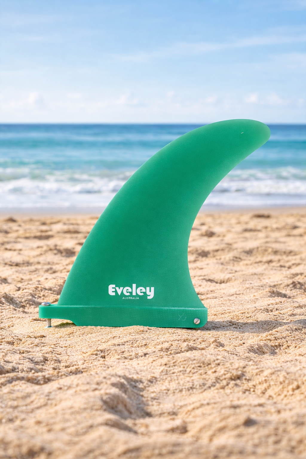Green Eveley 6.5-inch Classic center surfboard fin standing in sand with ocean waves in background.