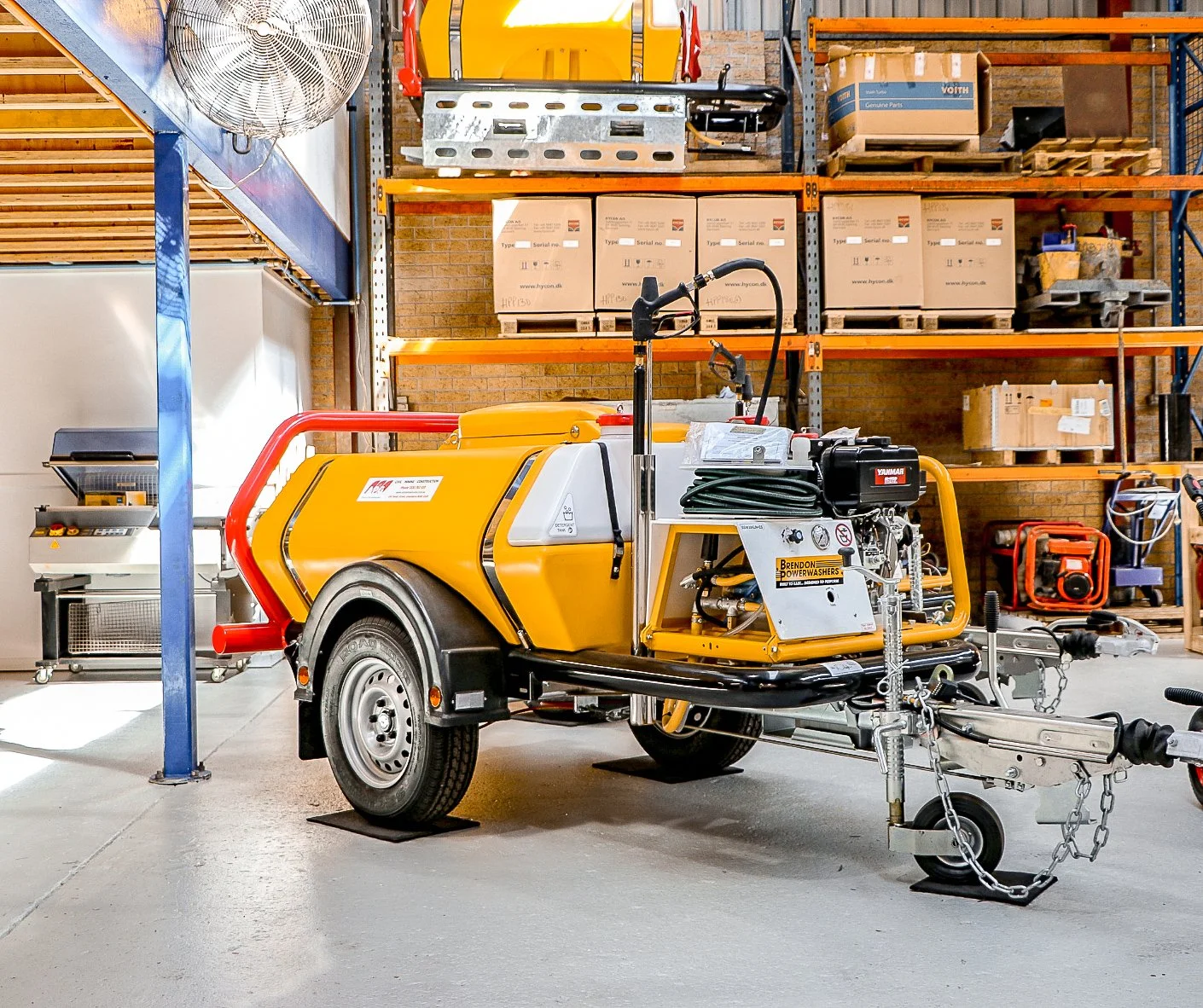 Yellow industrial trailer with equipment in a workshop with wooden shelves, boxes, and other machinery.