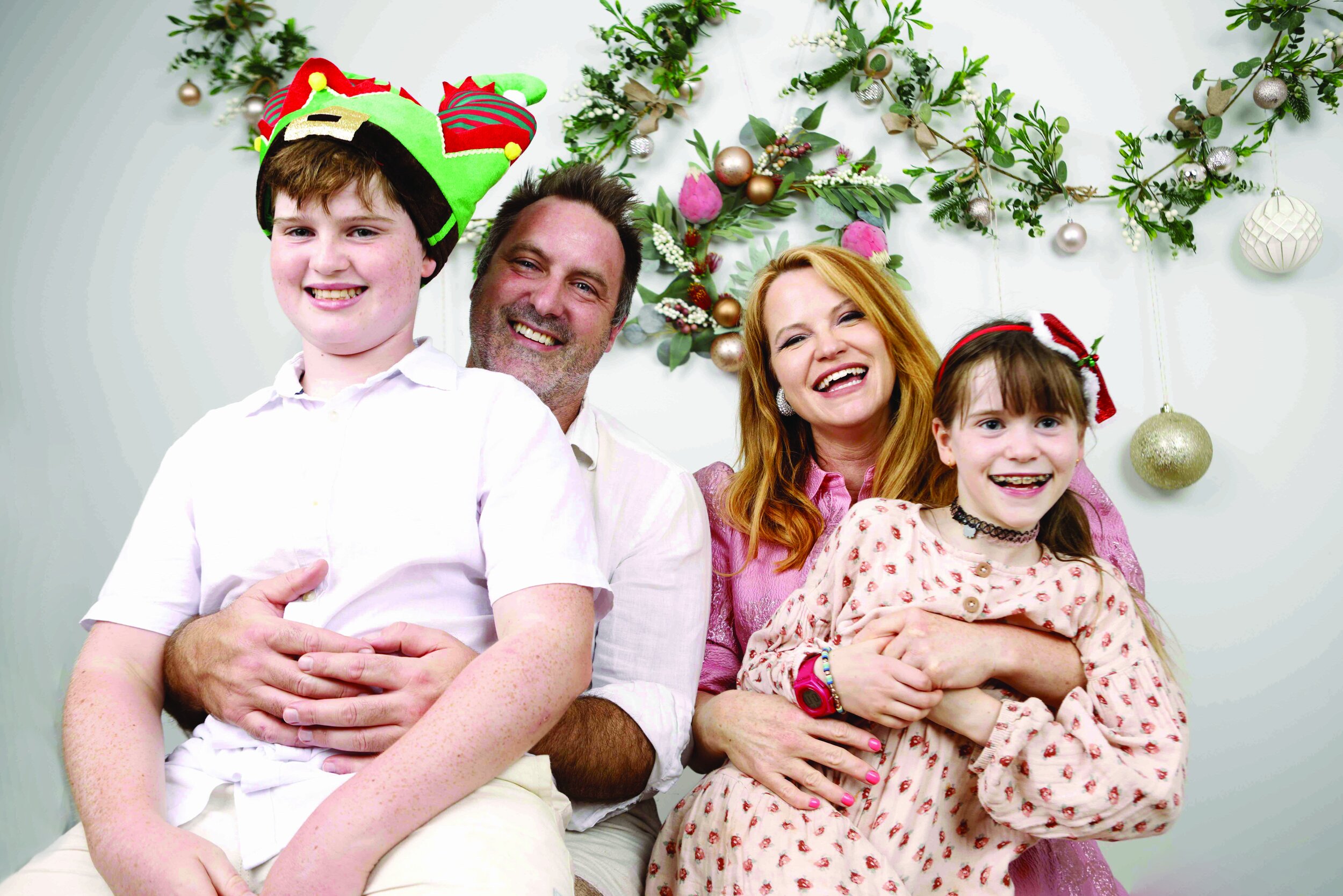 A smiling family of four celebrating the holidays, with festive hats and a decorated background.