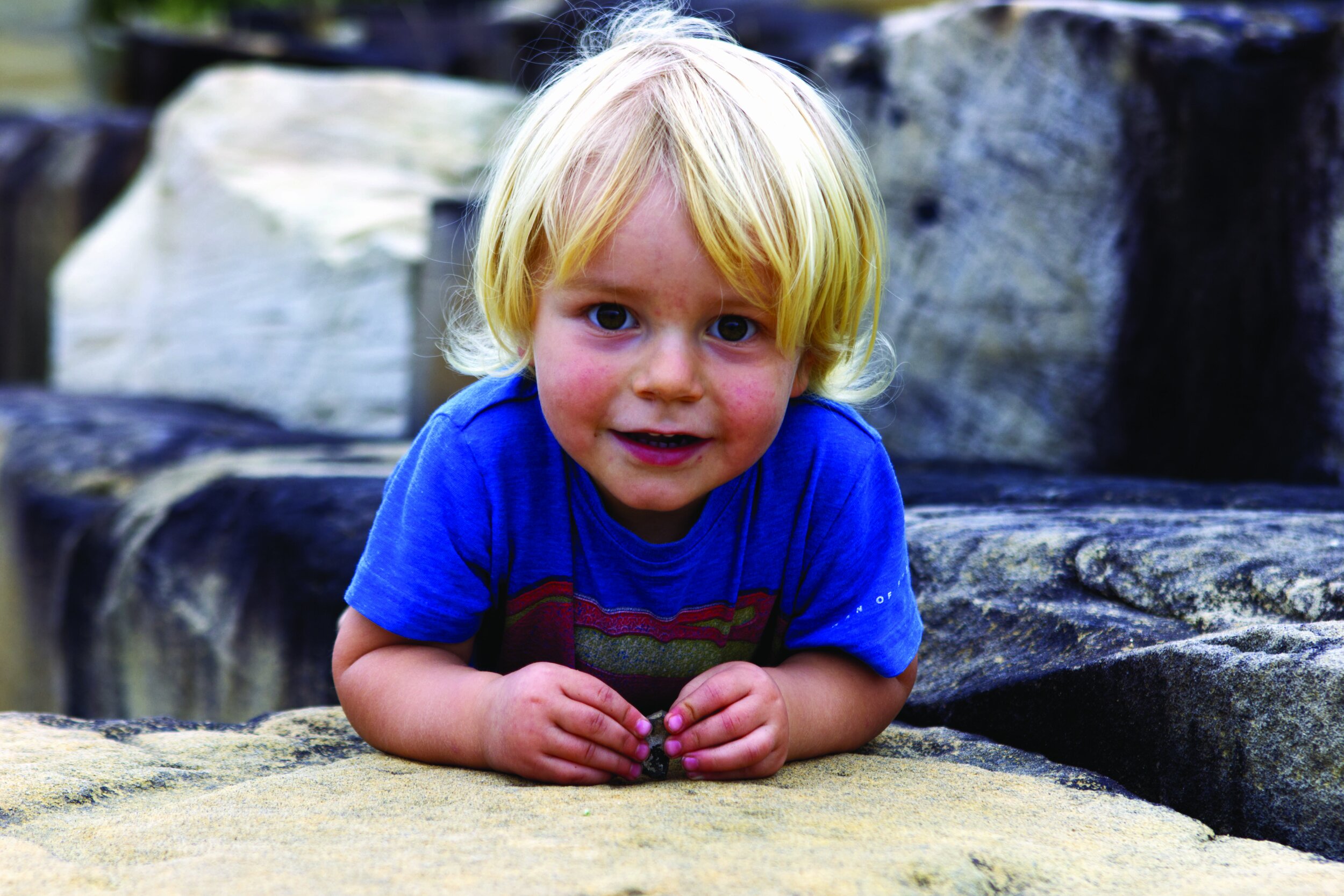 Blonde toddler in blue shirt on stone surface