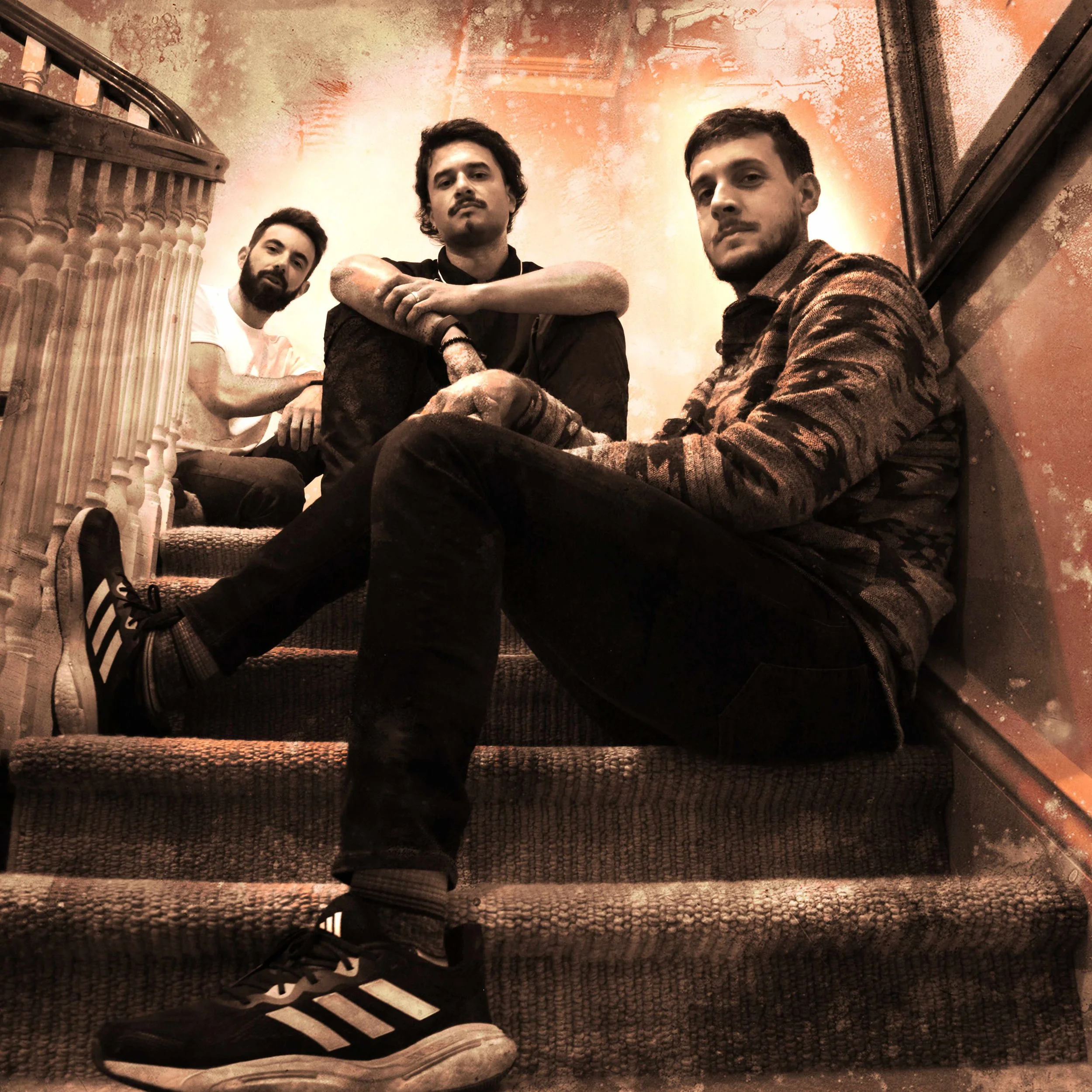 Three men sitting on a staircase, posing for the photo, with a painted wall in the background.