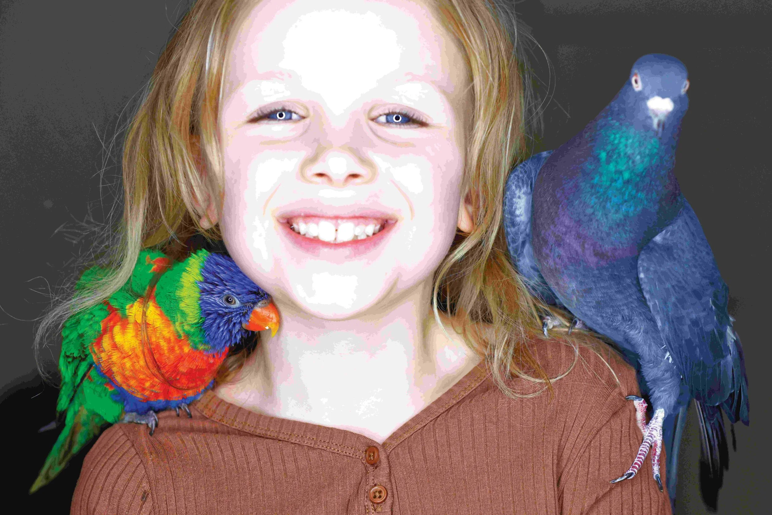 A young girl smiling with a colorful parrot on her shoulder and a large blue bird perched on her other shoulder.