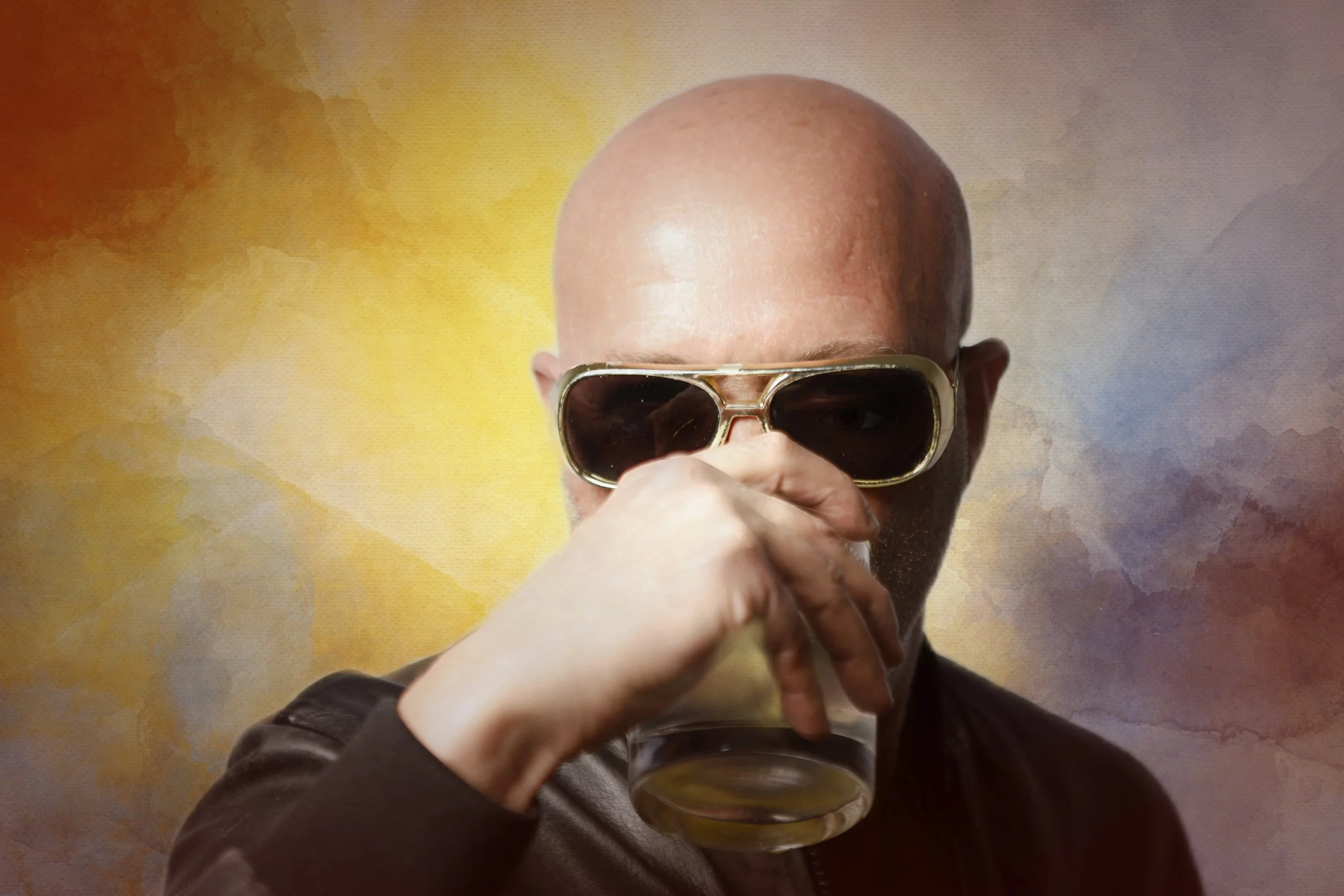 A bald man wearing sunglasses is holding a glass of beer near his mouth, with a colorful abstract background.