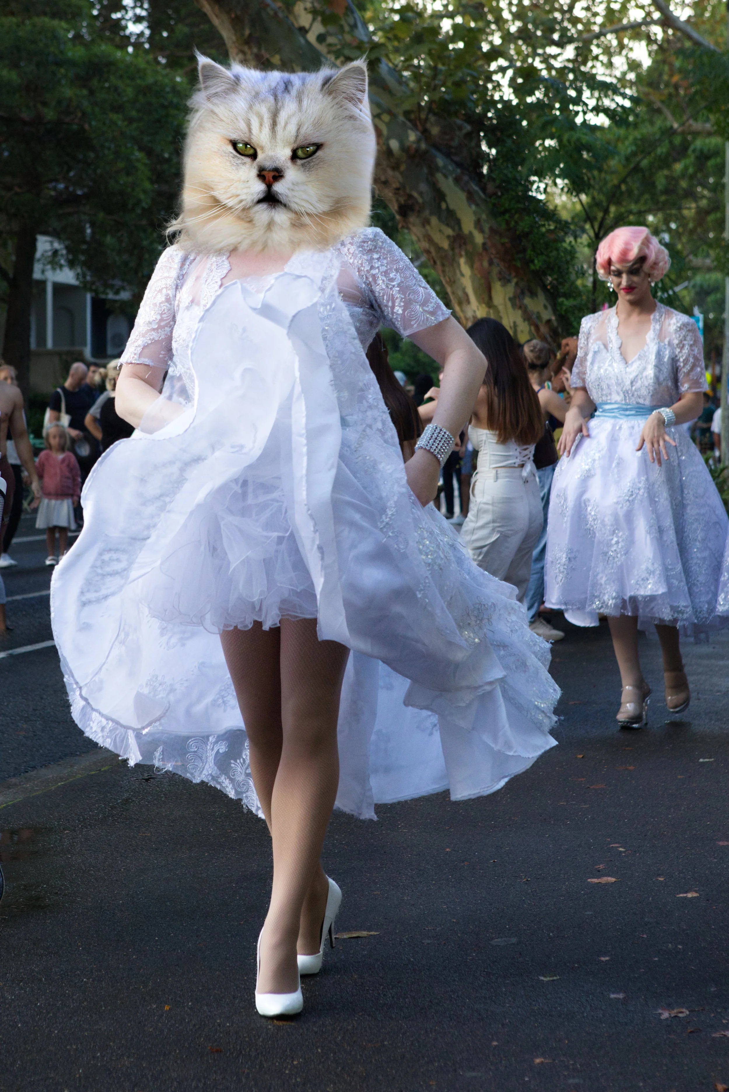 Person with a cat face wearing a white dress at an outdoor event