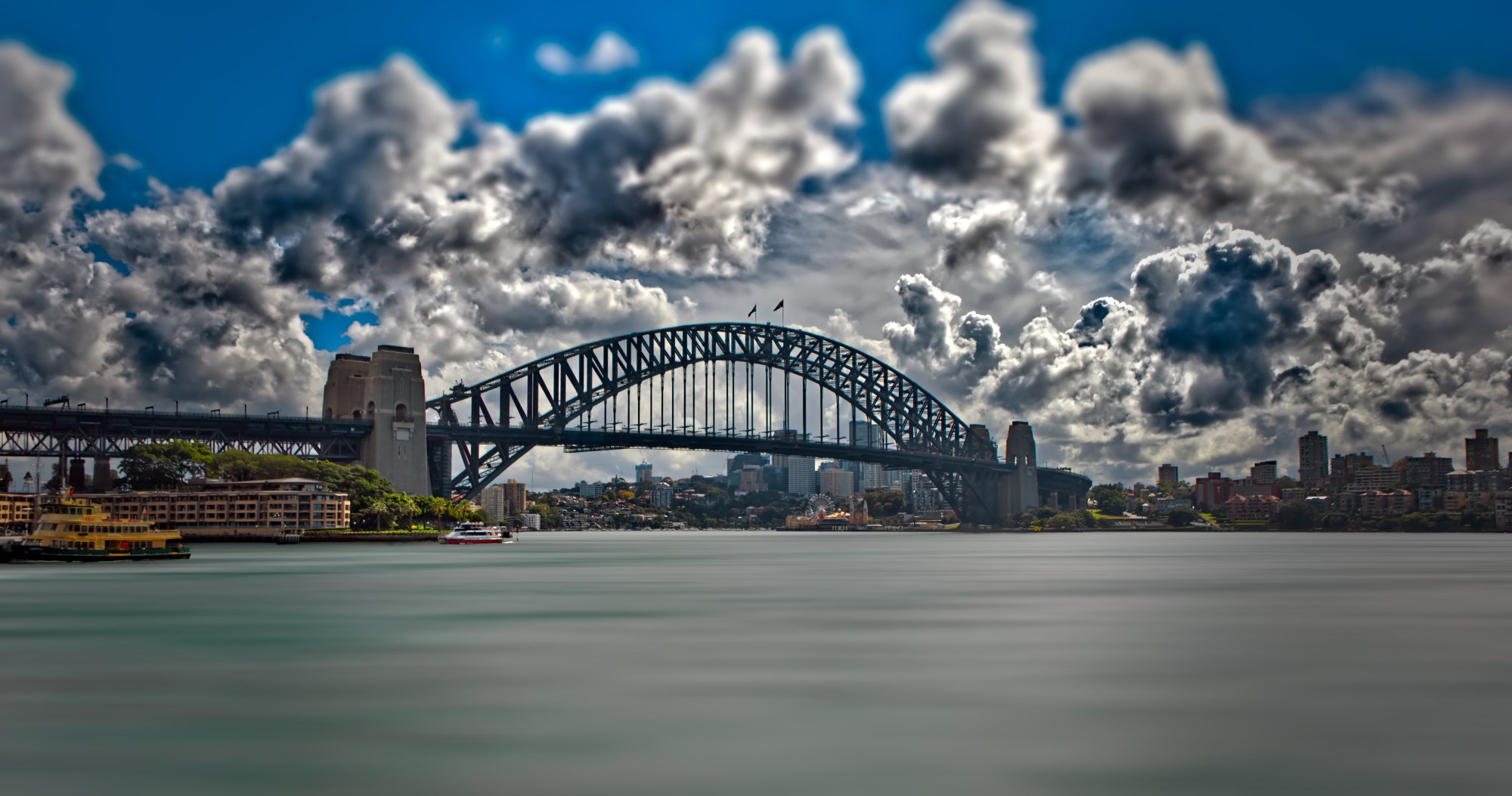 Sydney Harbour Bridge with cloudy sky and city skyline in the background.