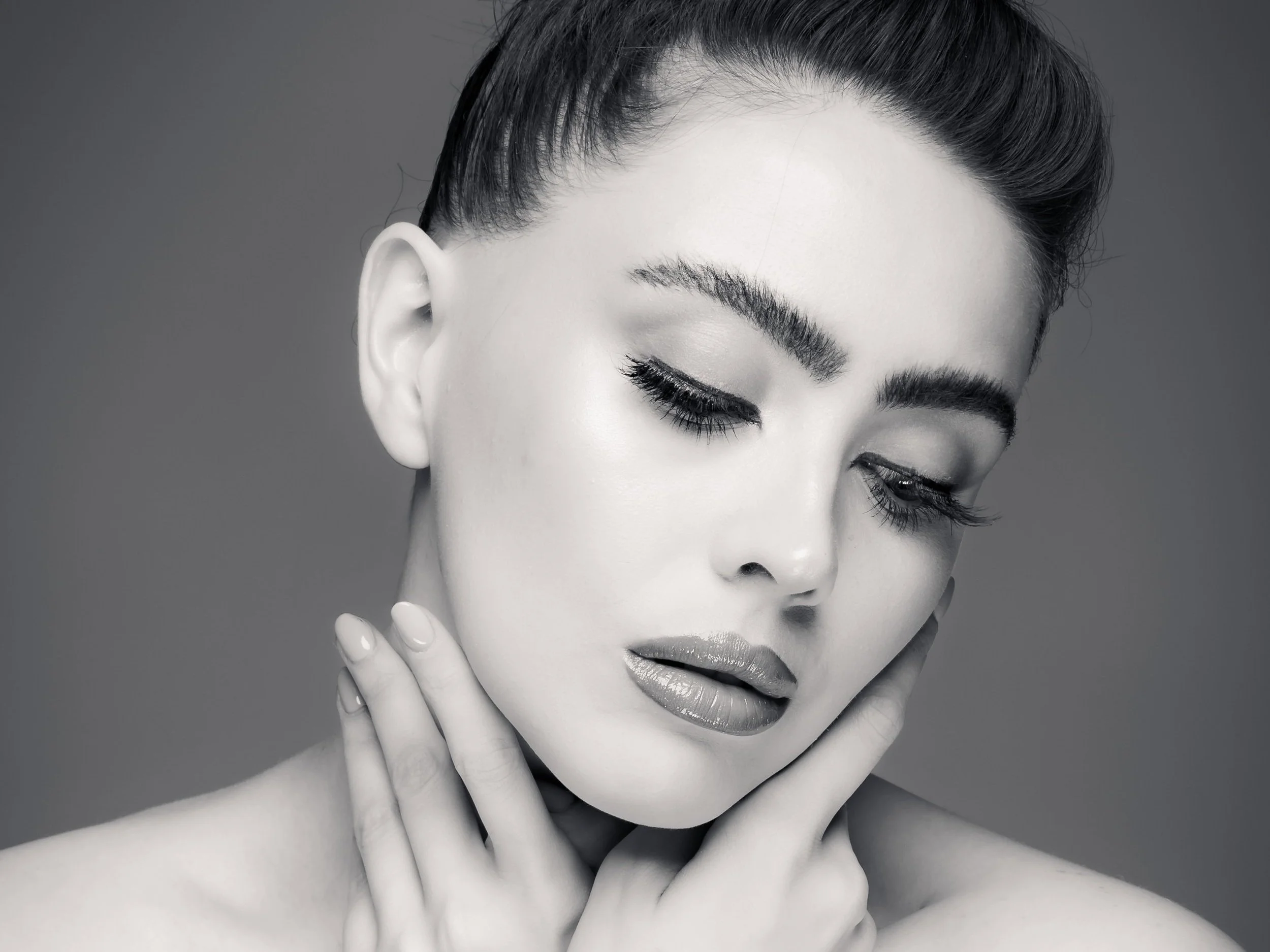 A black and white close-up photo of a woman with eyes closed, touching her face with her fingers, showing smooth skin and well-groomed eyebrows. Portrait by butterflies k-photography Thetford.
