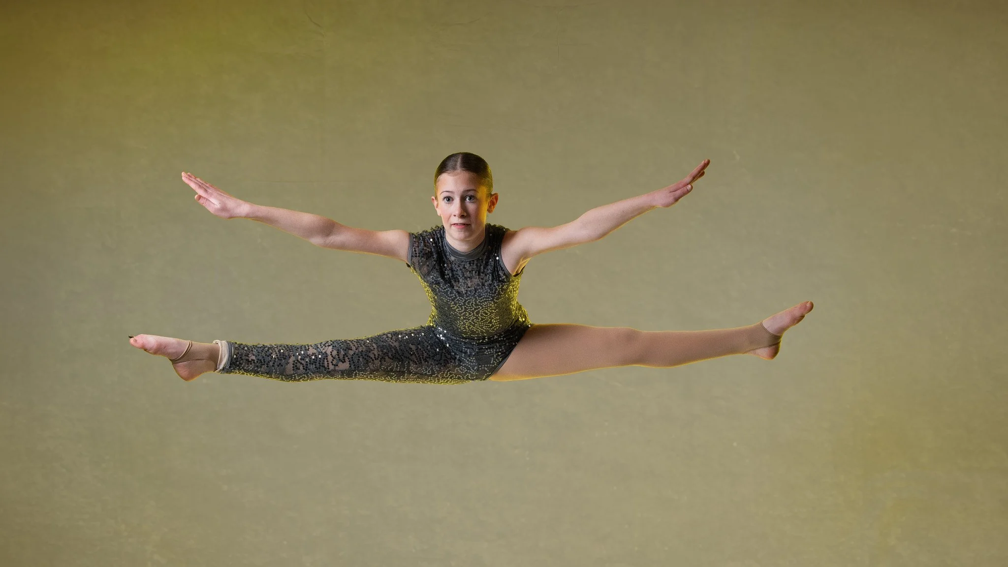 Girl in a sparkly leotard performing a split leap in mid-air with arms extended outward. Thetford dance photography by butterflies k-photography.