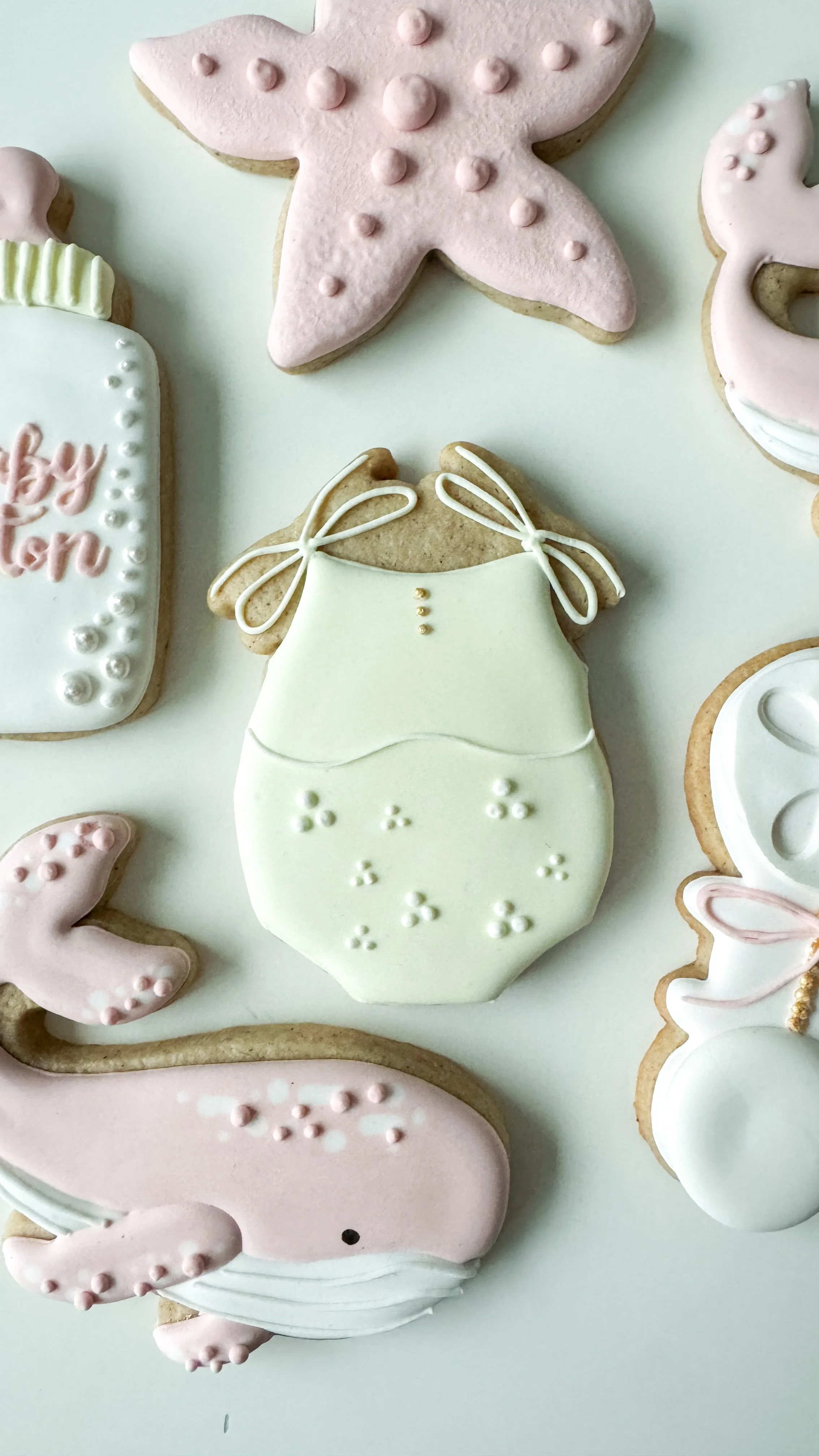Onesie cookie as part of a baby shower pastel theme with whales, bottle, rattle, and starfish.