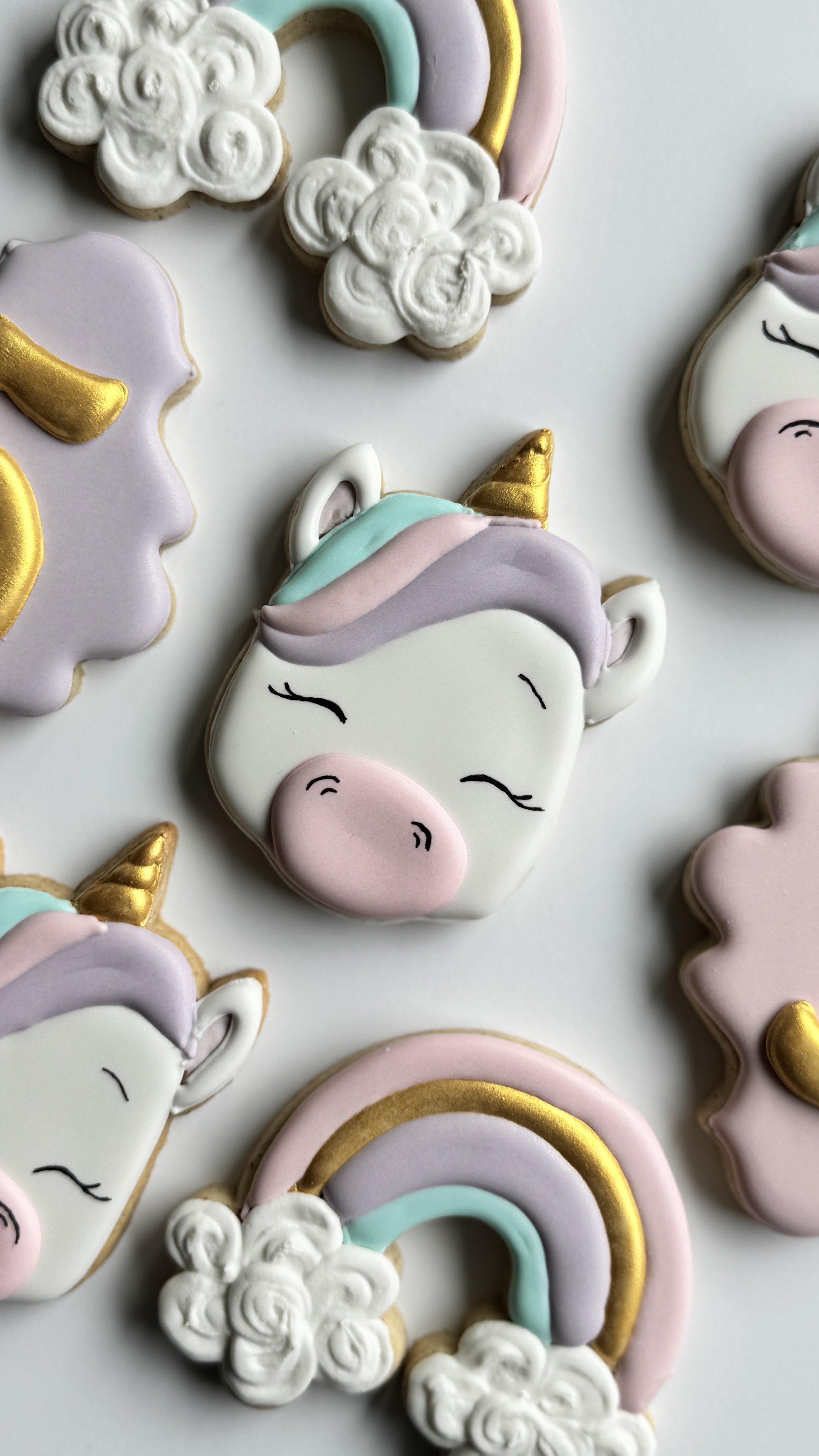 Decorated unicorn-themed cookies with rainbow cookie in light pink, teal, purple, white, and gold. 