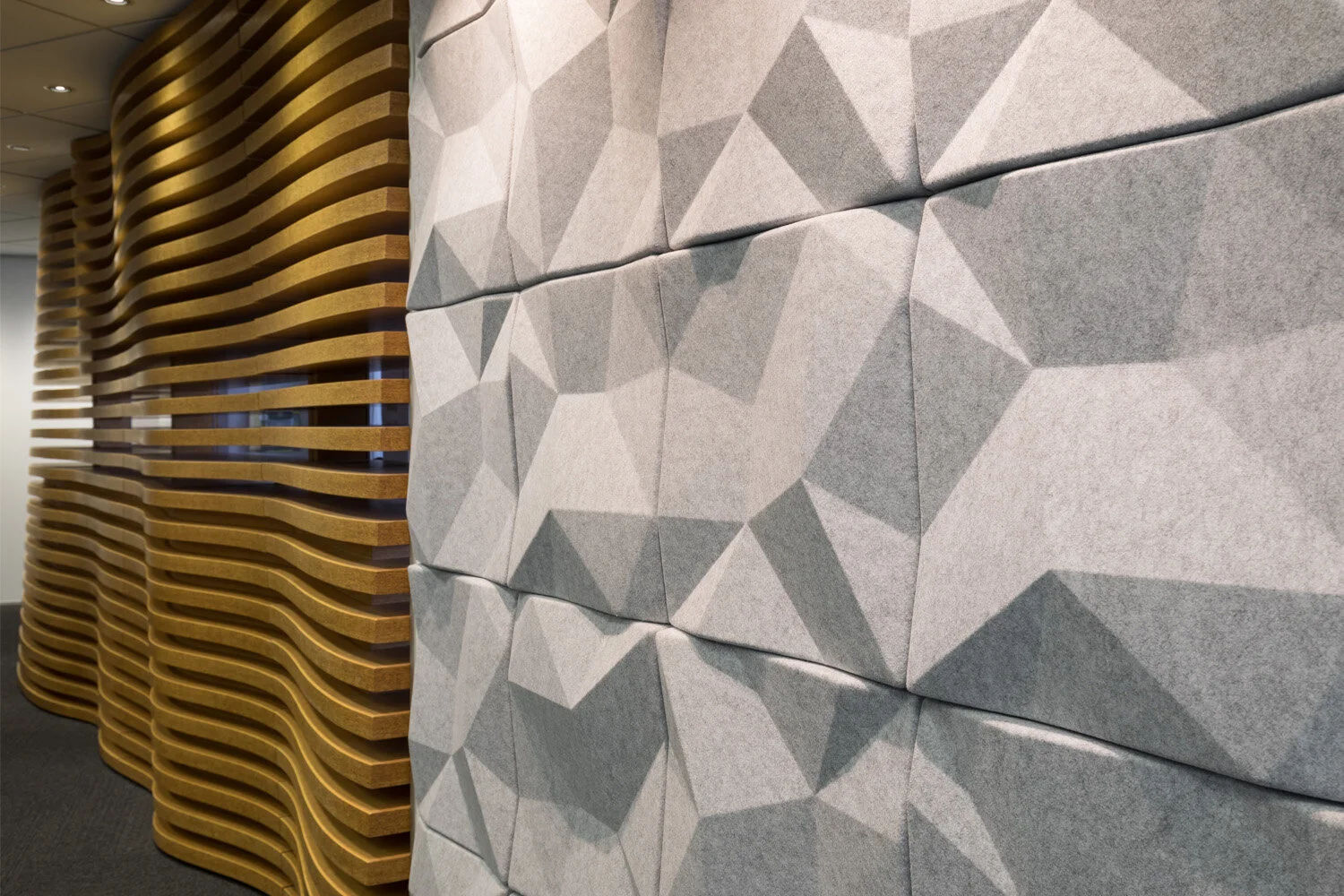 Close-up of a modern interior wall featuring textured 3D geometric gray panels on one side and curved wooden slats on the other side.