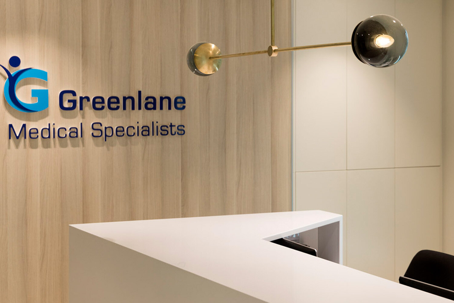 Reception area at Greenlane Medical Specialists with a wooden wall, modern light fixture, and a white desk.