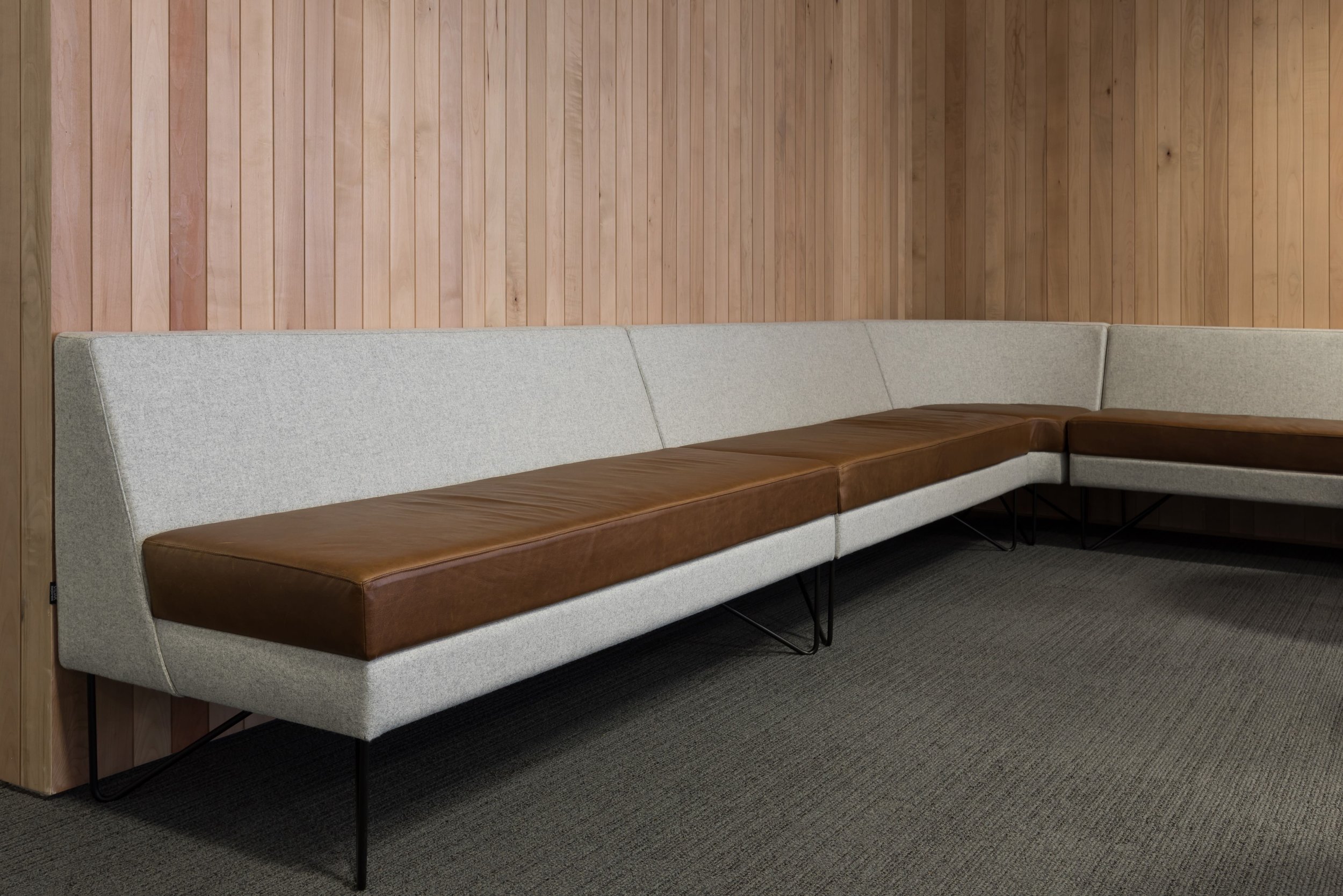 A modern sectional sofa with light gray fabric and brown leather cushions against a wood-paneled wall.