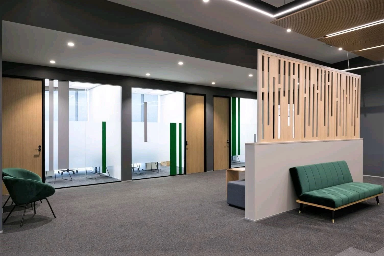 Modern office lobby with green chairs, sitting area, glass-walled conference rooms, wooden doors, and a wooden partition divider.