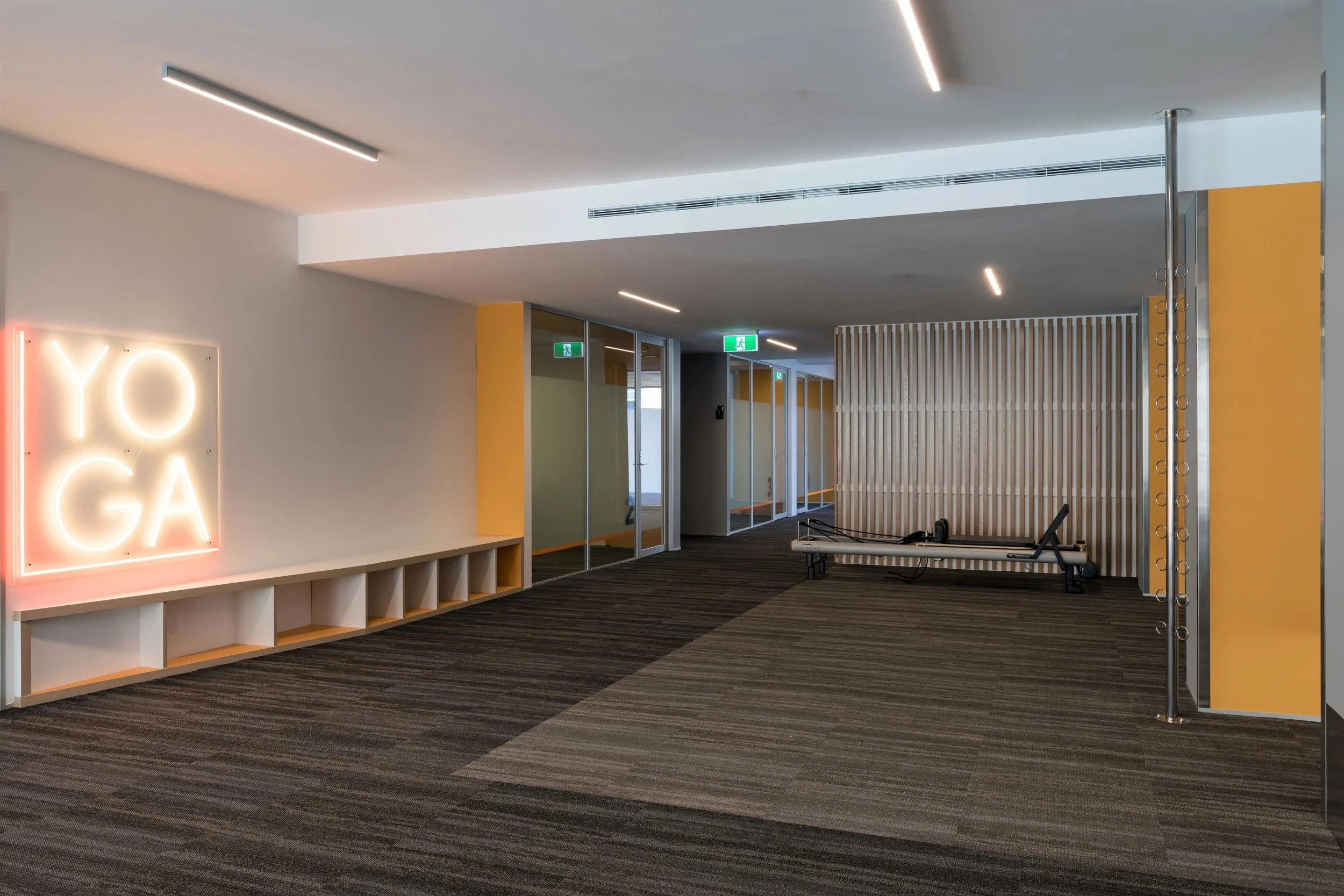 Modern fitness studio or yoga room with neon 'YOGA' sign, mirrored wall, padded flooring, and workout equipment.