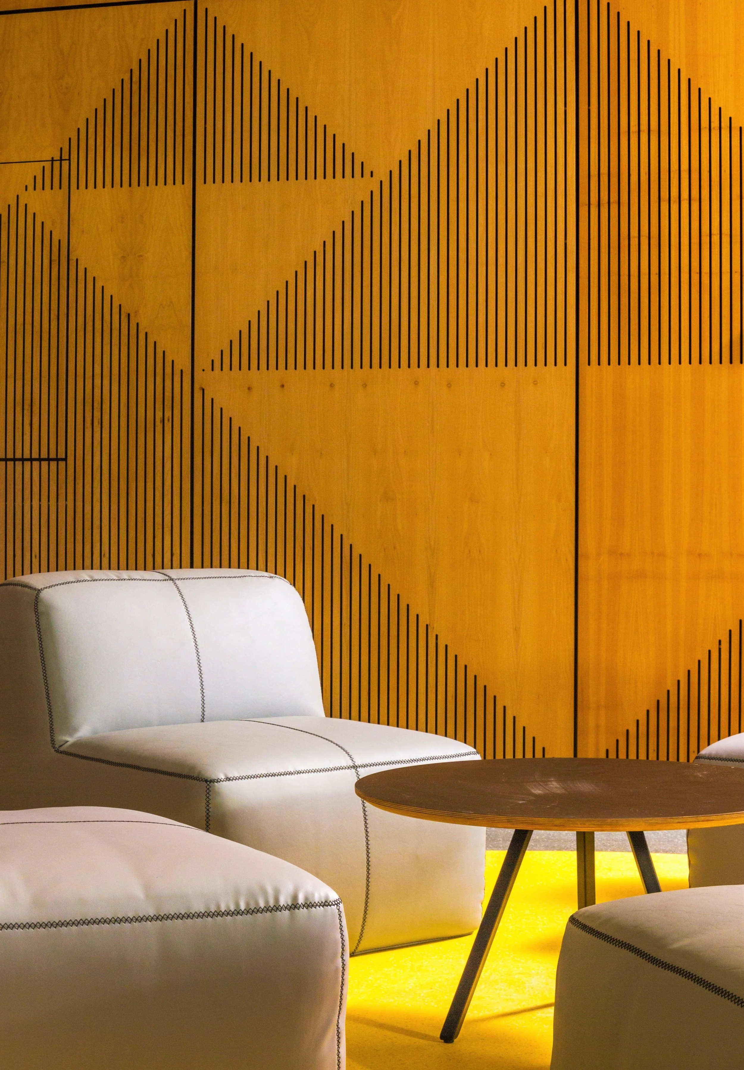 Modern room with white armchairs, wooden coffee table, yellow carpet, and a wooden wall with geometric black line patterns.