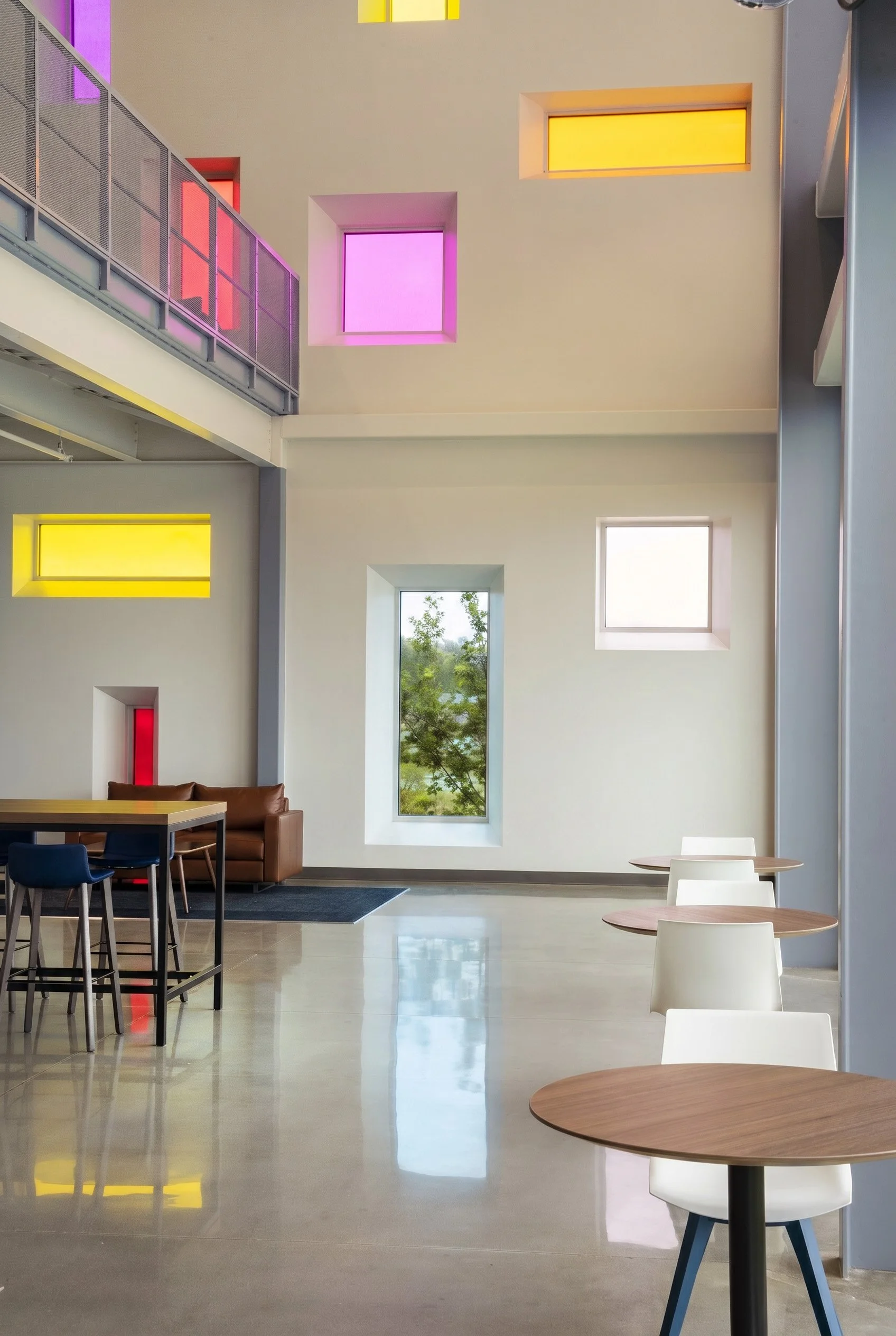Modern interior space with various colored windows, table, chairs, and a leather sofa.