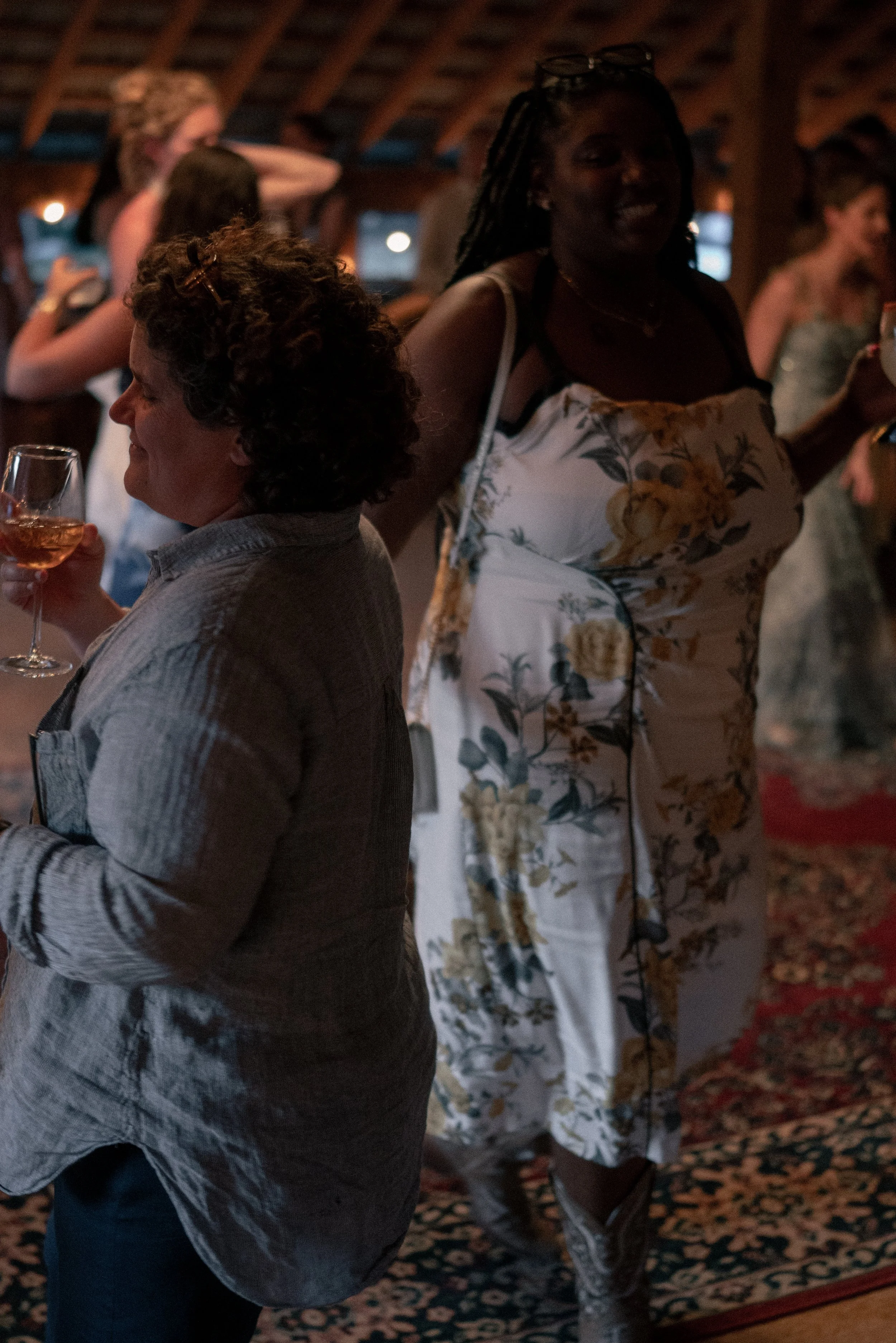 People socializing at an indoor gathering or party, with one woman holding a glass of rosé wine, others in the background chatting and smiling.