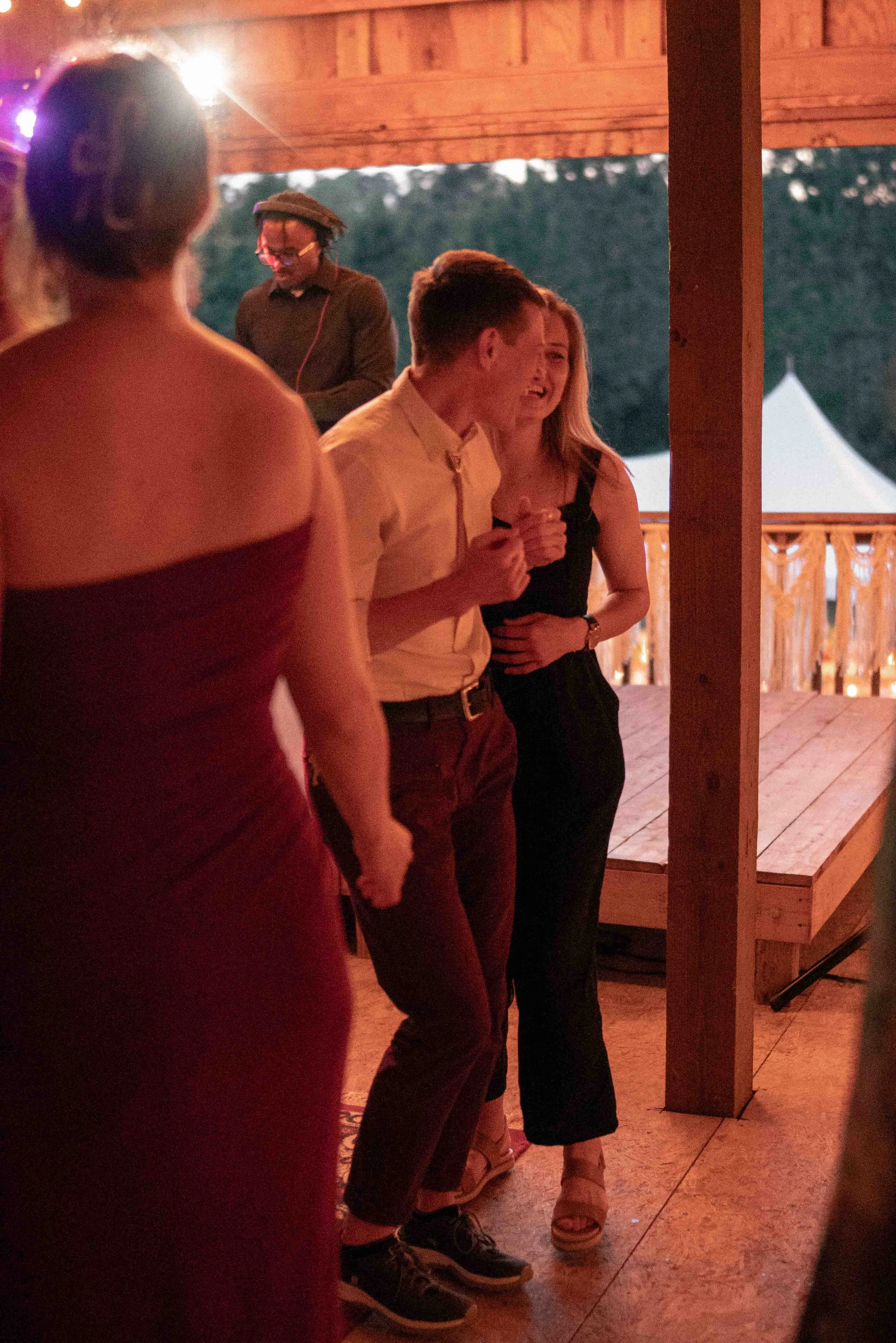 Group of young people at a social gathering, dancing and enjoying themselves under a wooden pavilion at dusk.