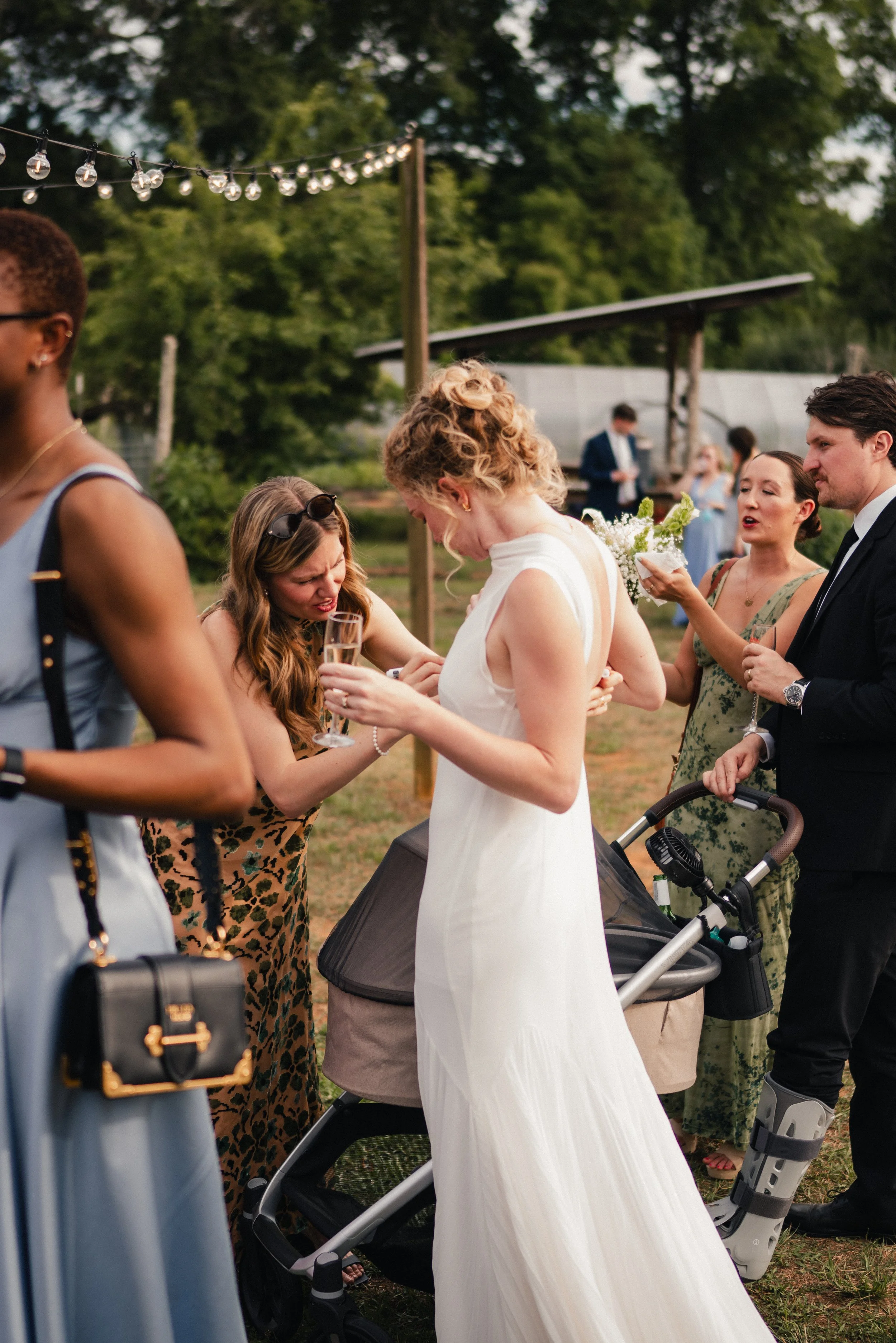 Group of people at outdoor wedding reception, bride in white dress exchanging vows or rings with bride in leopard print dress, guests around, trees and string lights in background.
