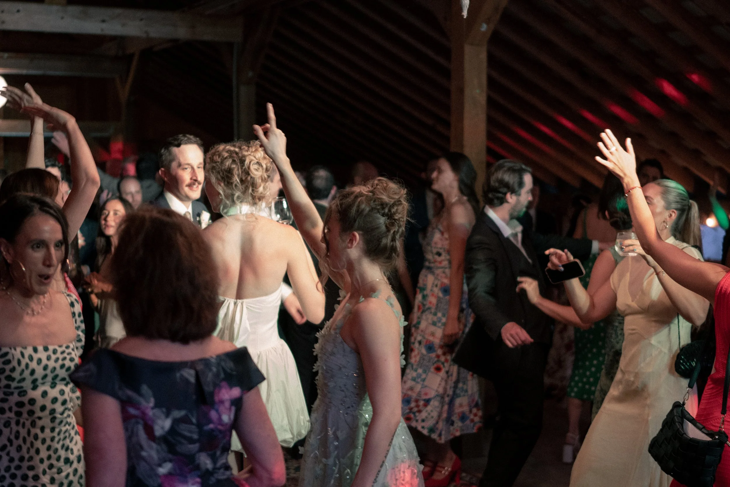 People dancing and socializing at a party in a decorated indoor space with wooden ceiling beams.