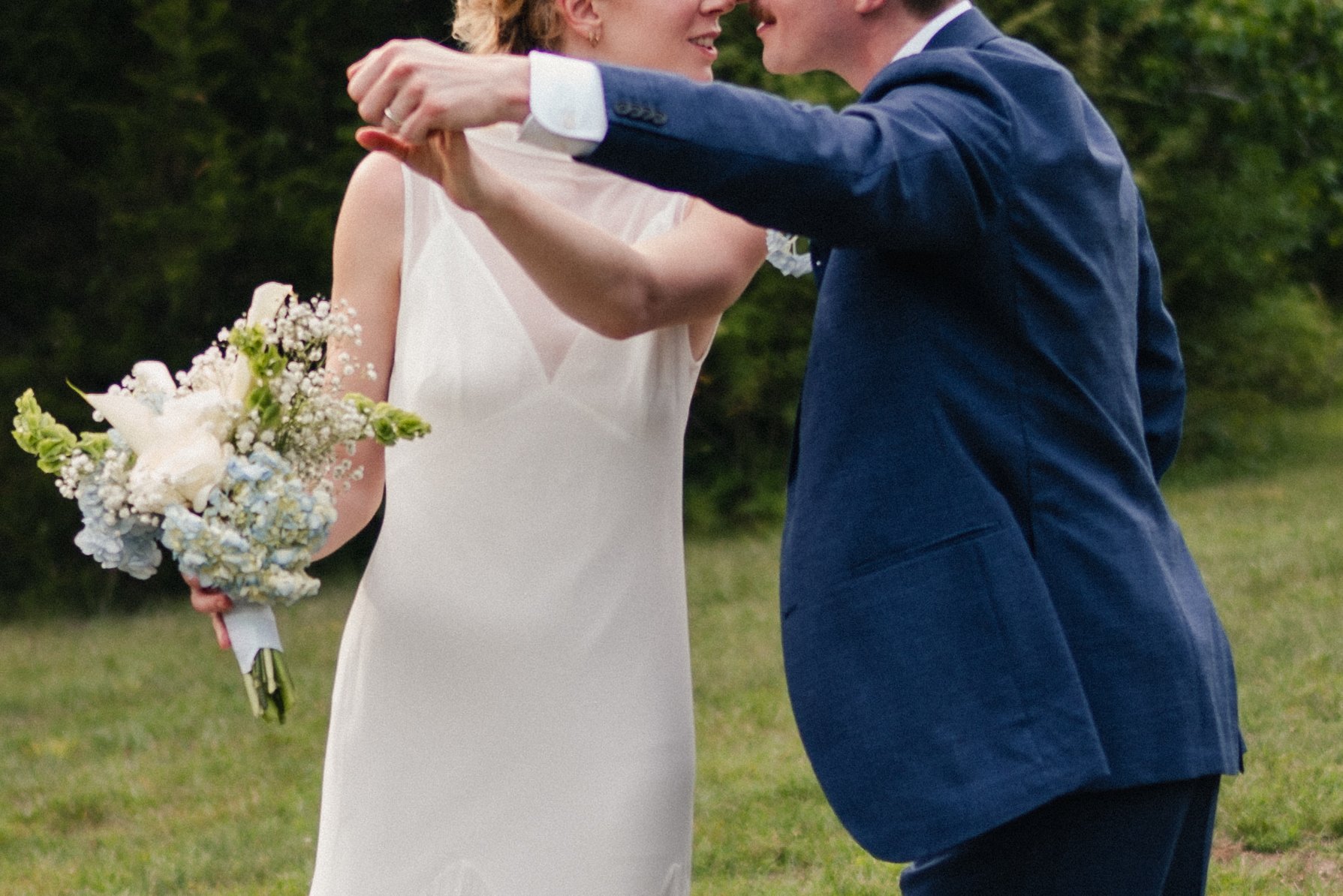 A bride and groom holding hands and dancing outdoors during their wedding celebration.