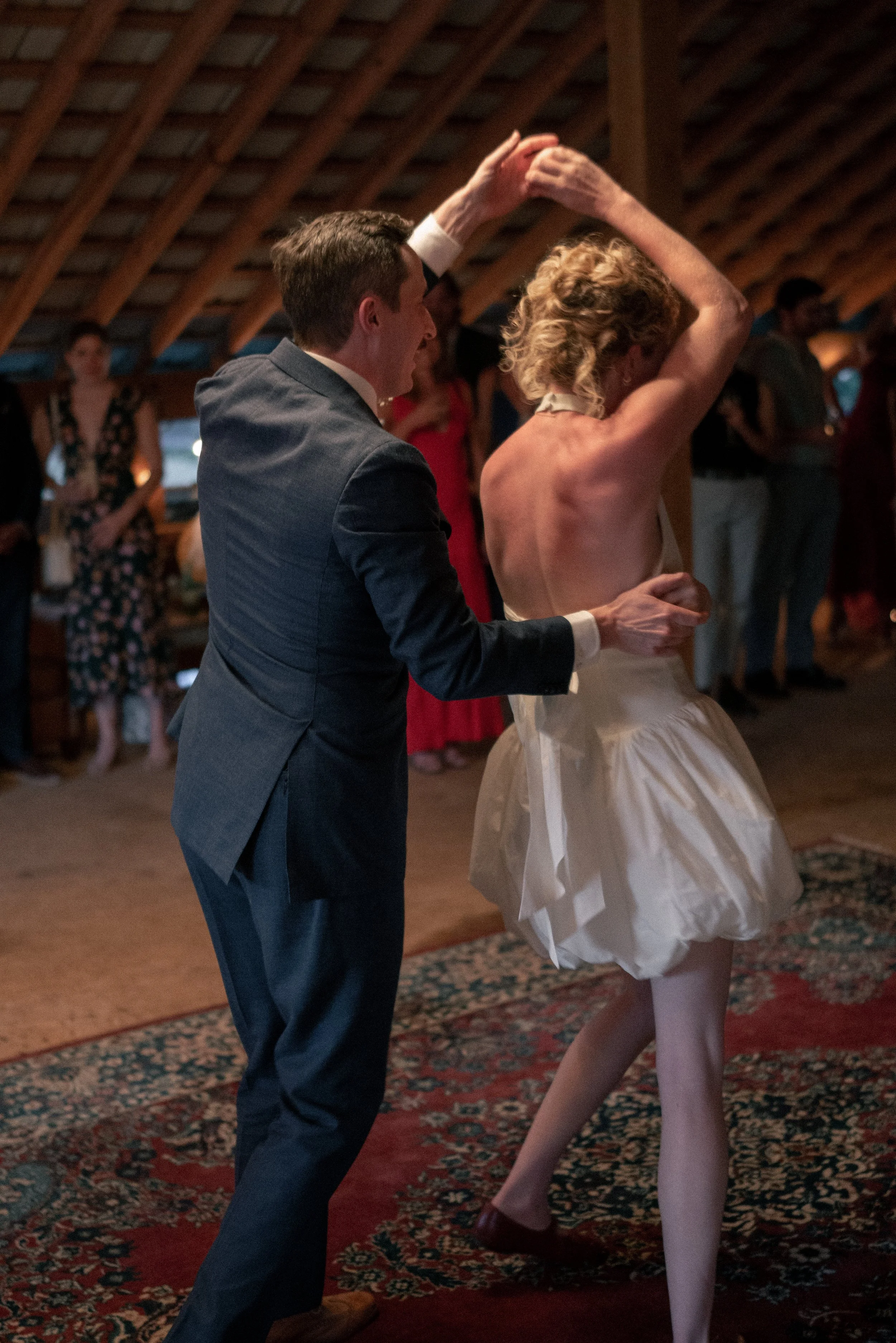 A man and a woman dancing together at a party or celebration, with other people in the background.