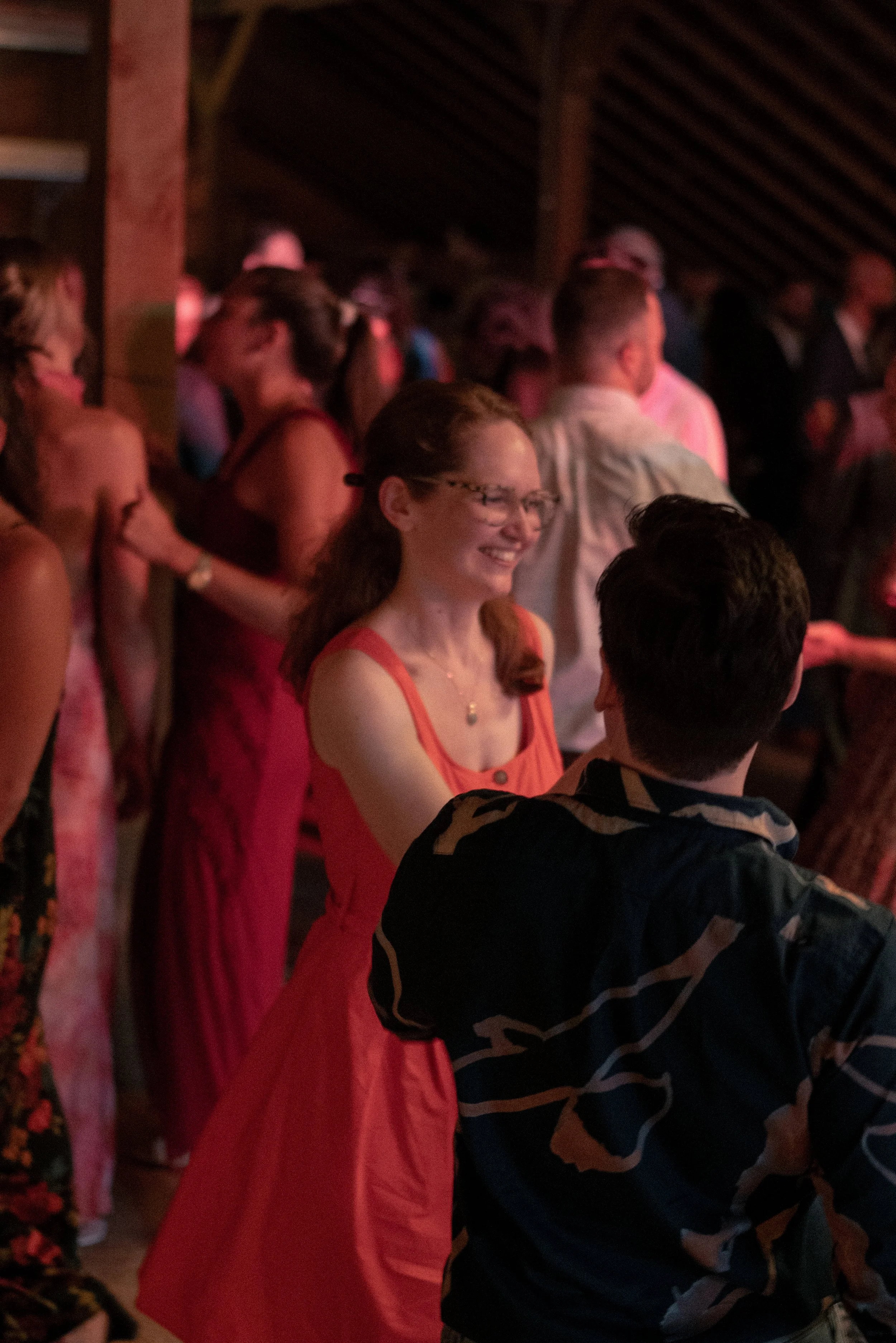 A crowd of people at a social gathering, some wearing formal attire, with warm lighting.