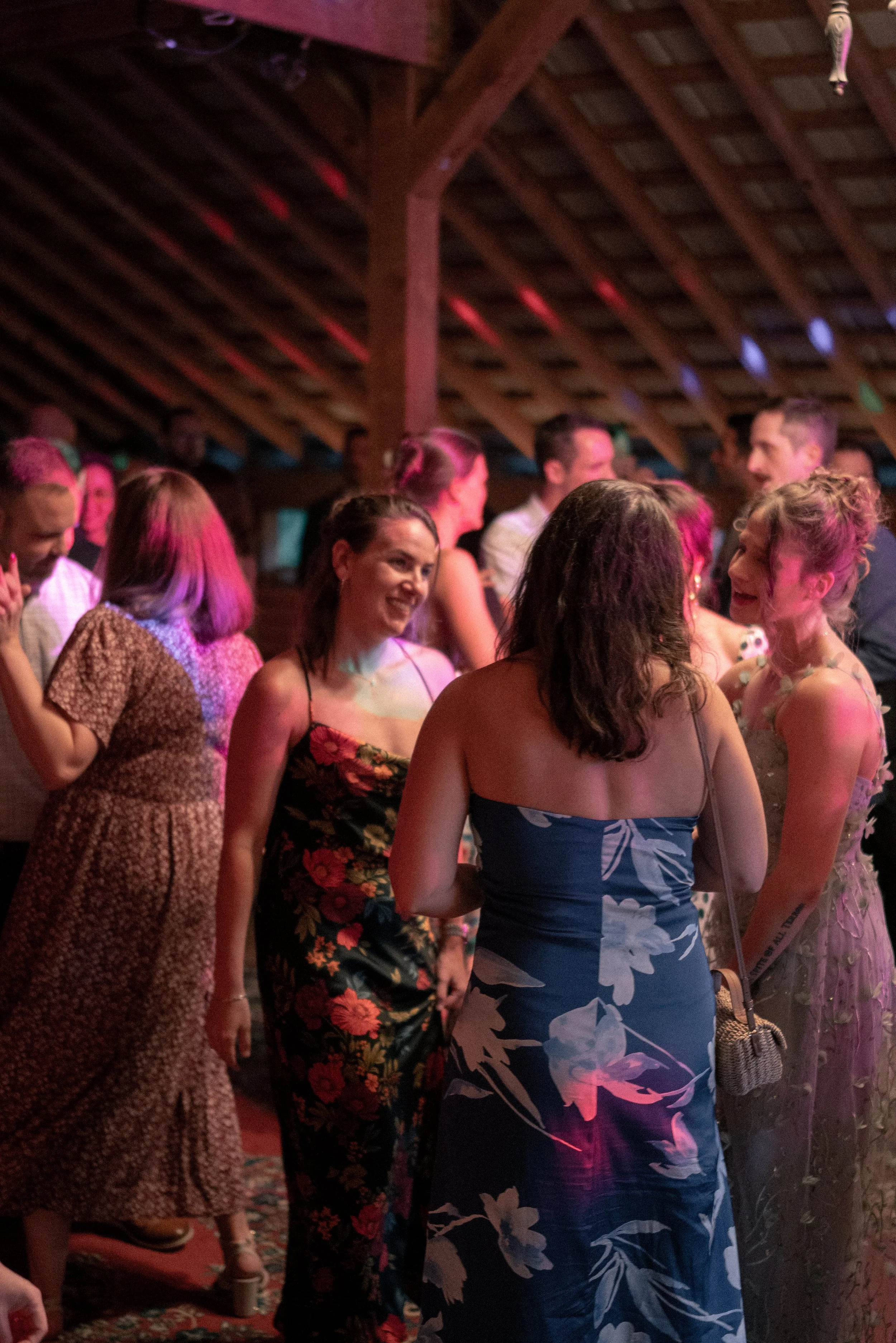 People dancing and socializing at a party or celebration in a rustic venue with wooden beams.
