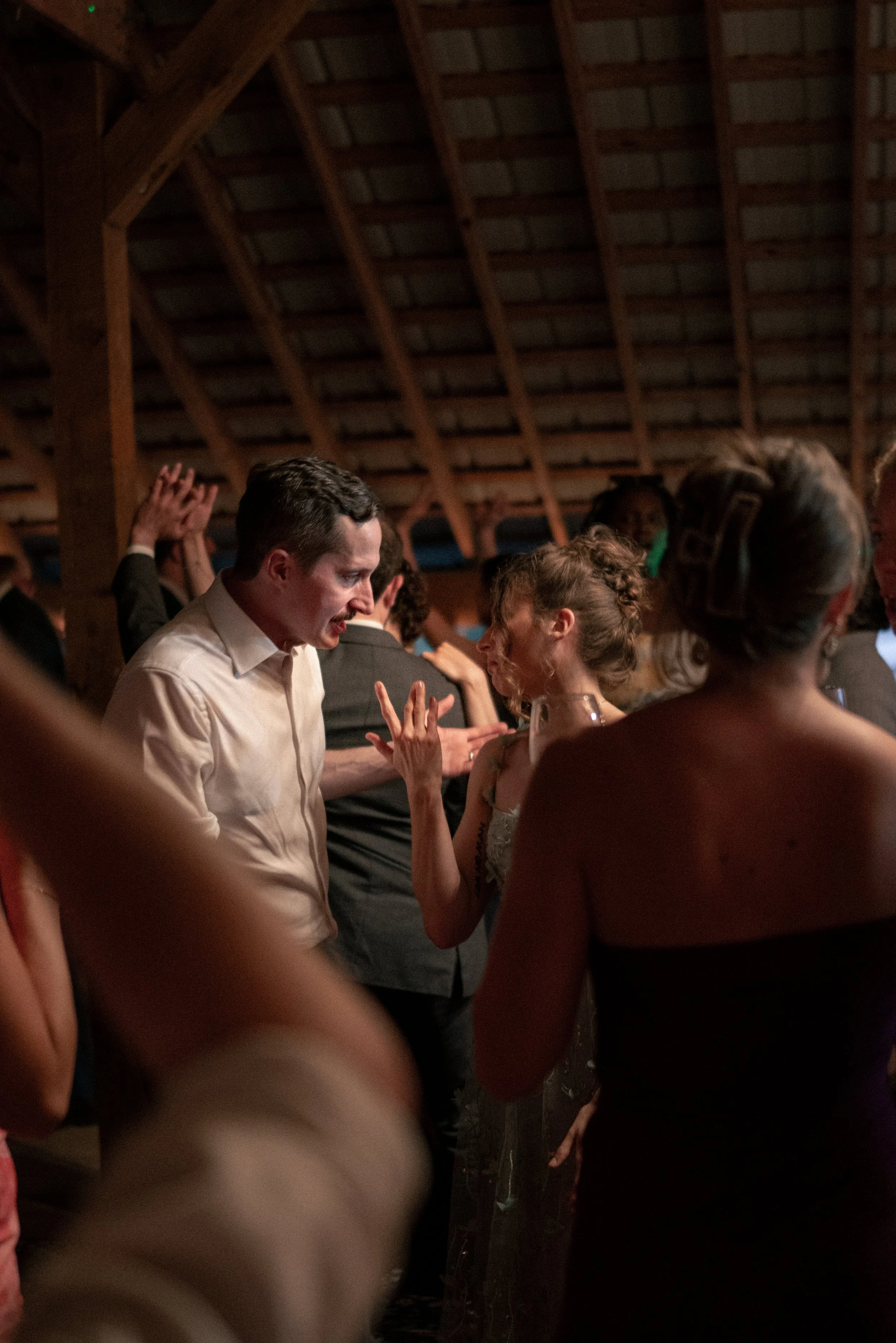 People at a gathering in a wooden venue, engaged in conversation and socializing, with some visible wearing formal attire.