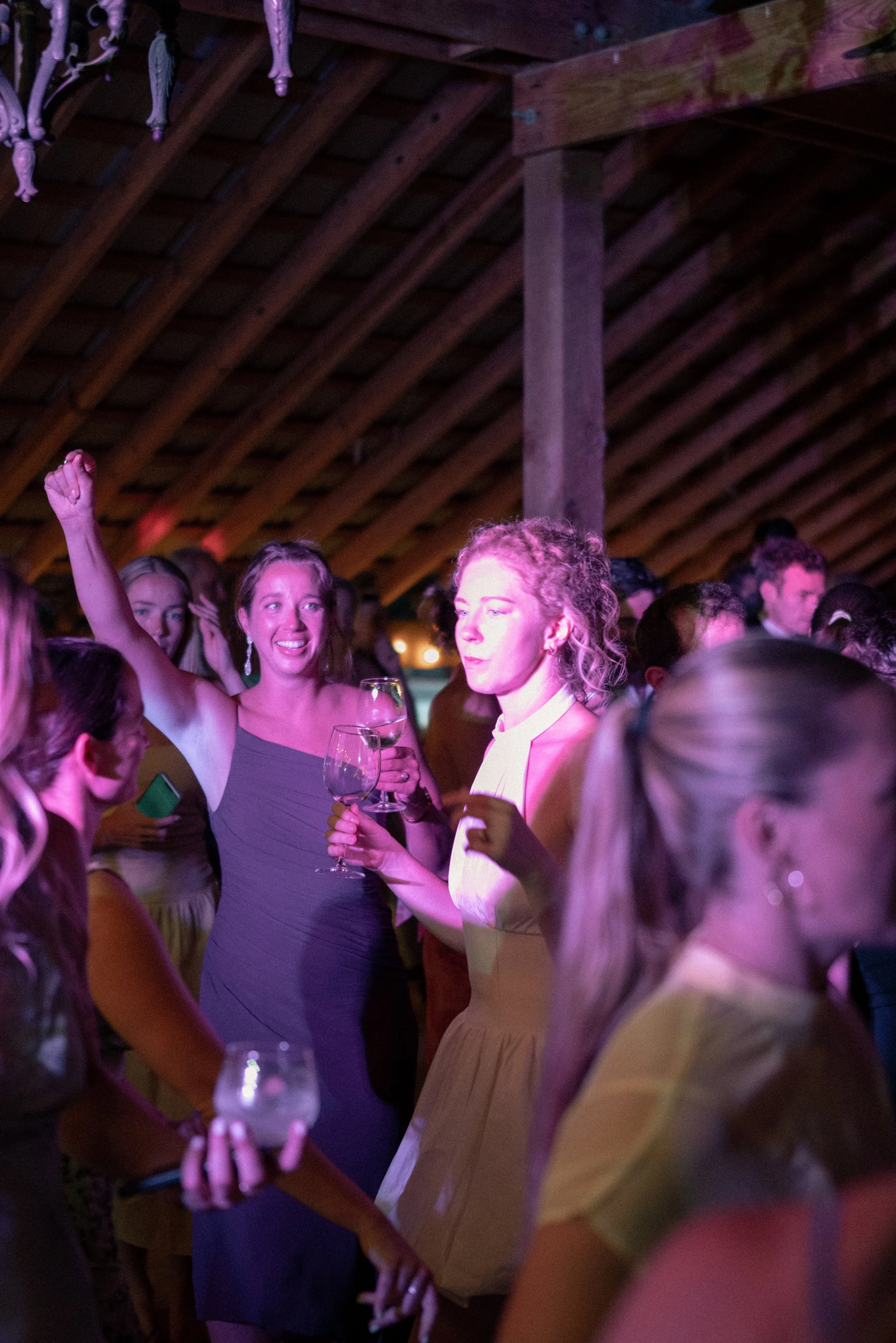 People at a social event in a dimly lit venue with a wooden ceiling, some holding glasses of wine, engaged in conversation and interaction.
