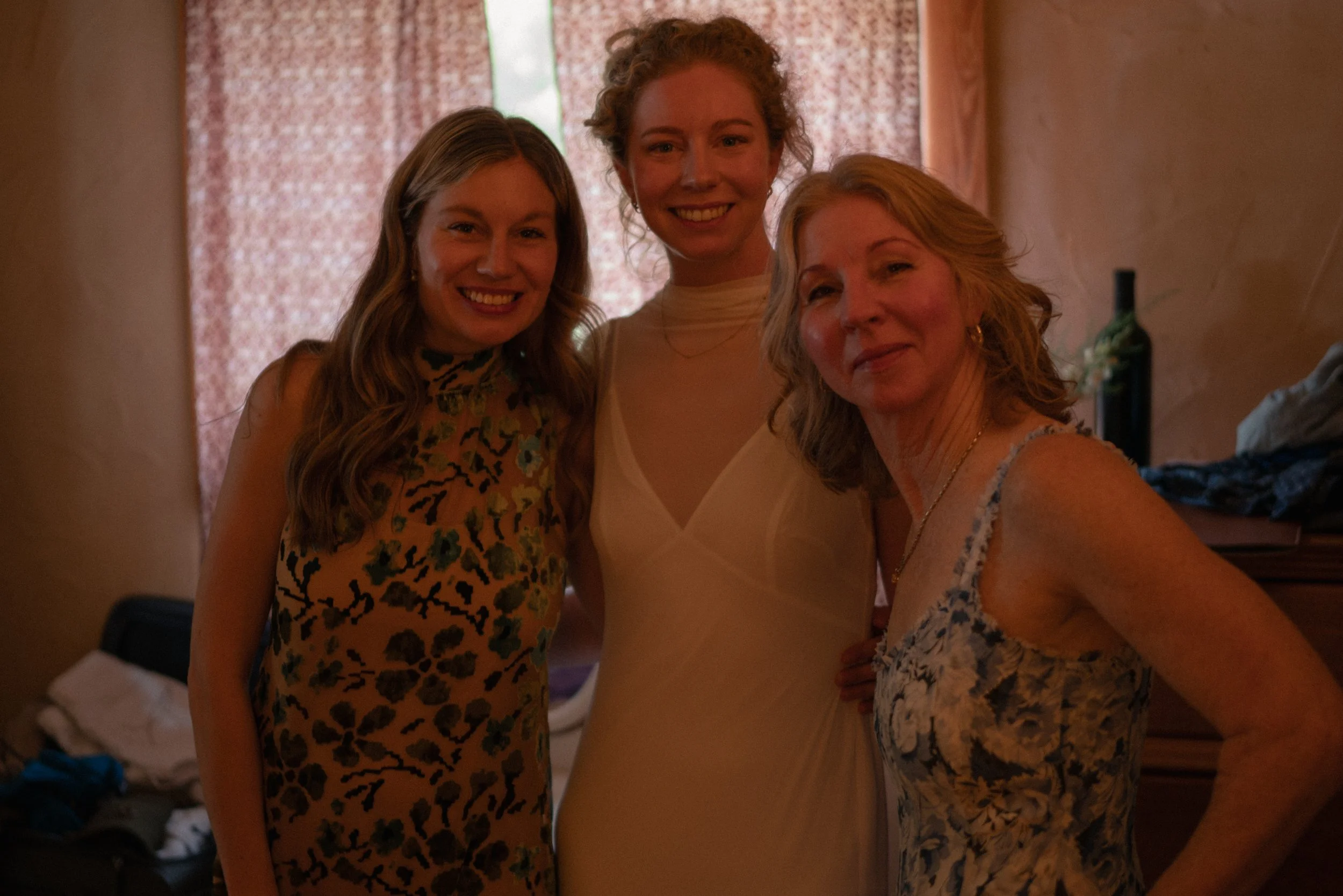 Three women standing close together indoors, smiling at the camera.