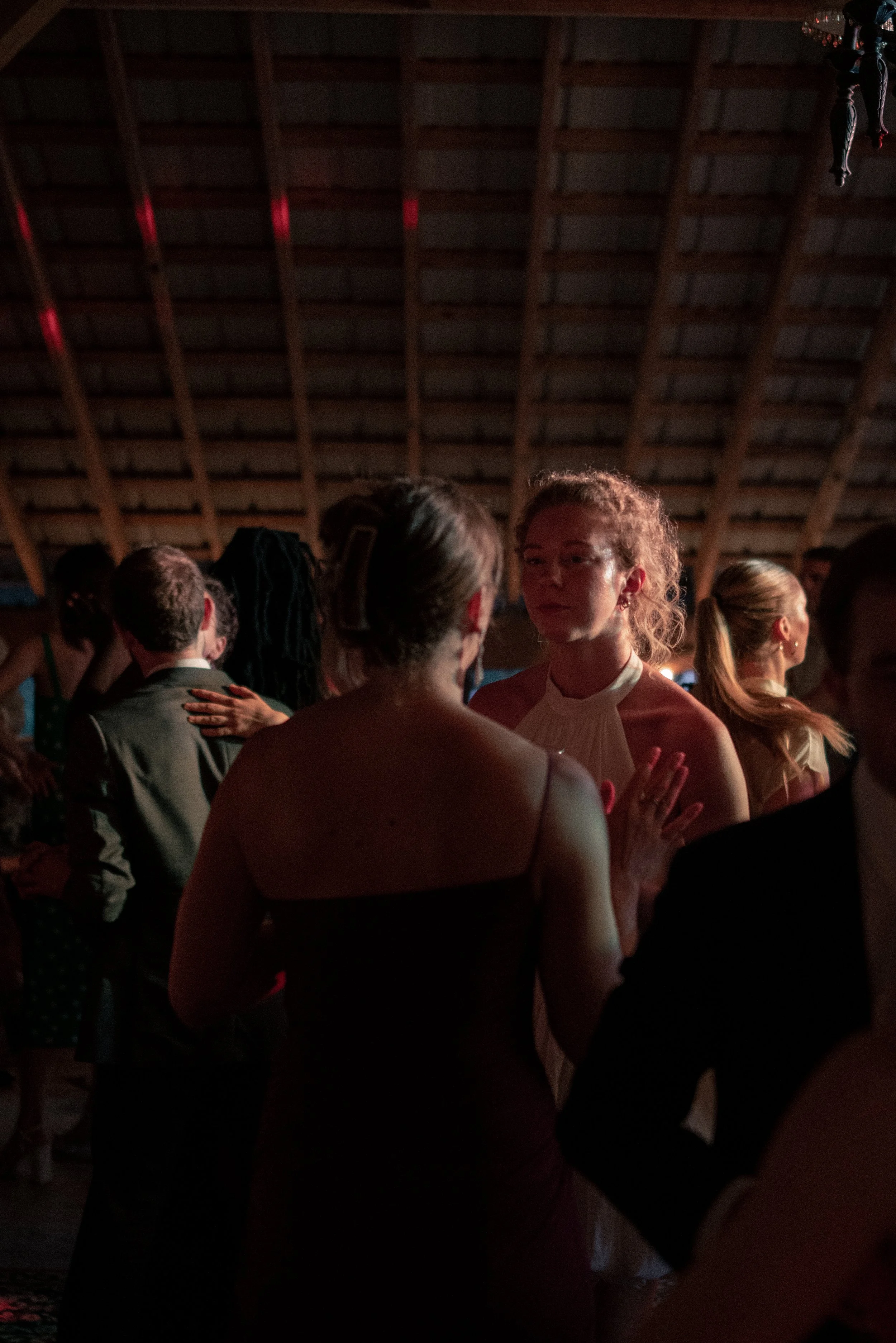 People dancing closely together at a dimly lit social event inside a venue with a wooden roof.