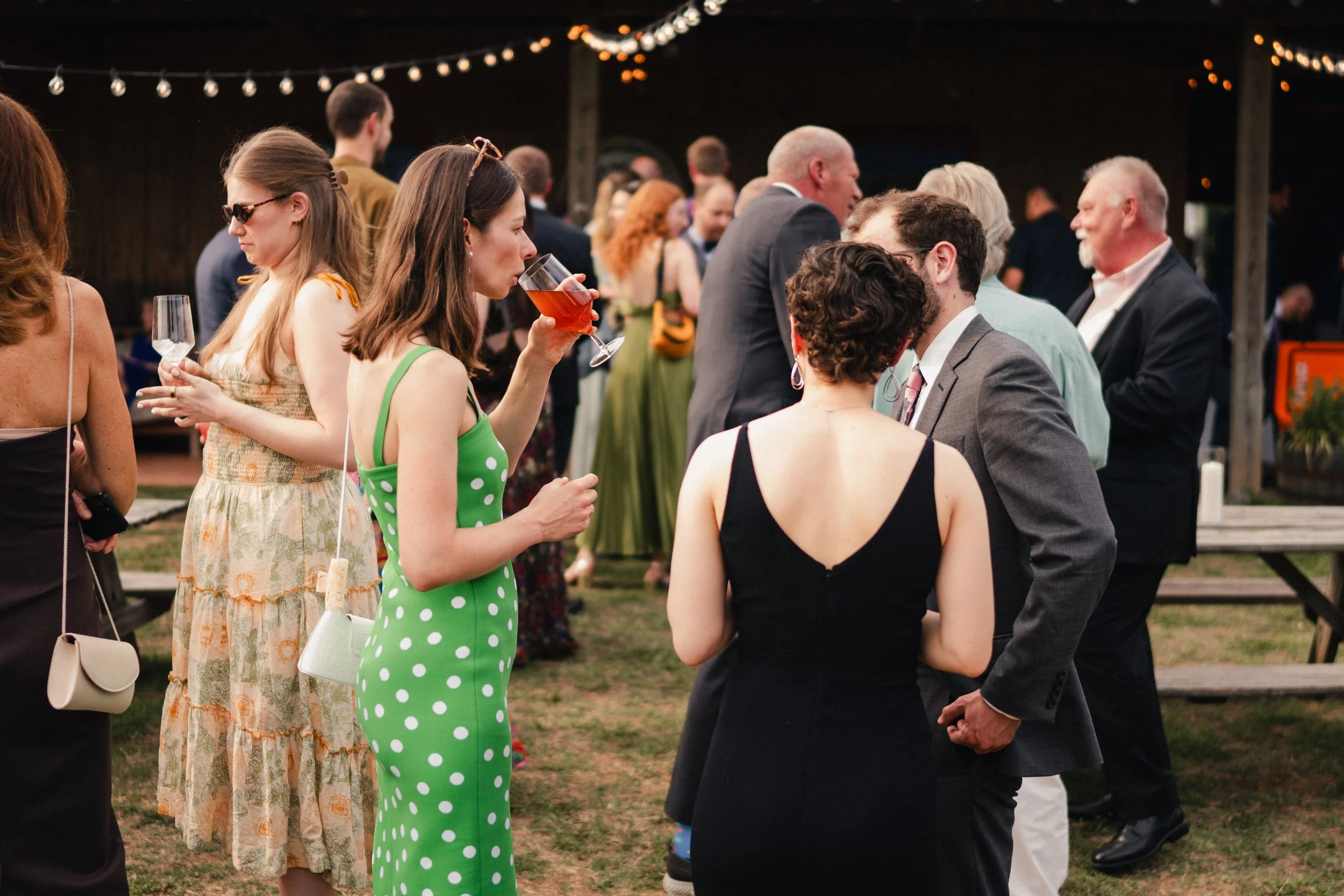 People socializing at an outdoor evening event under string lights, with some holding drinks.