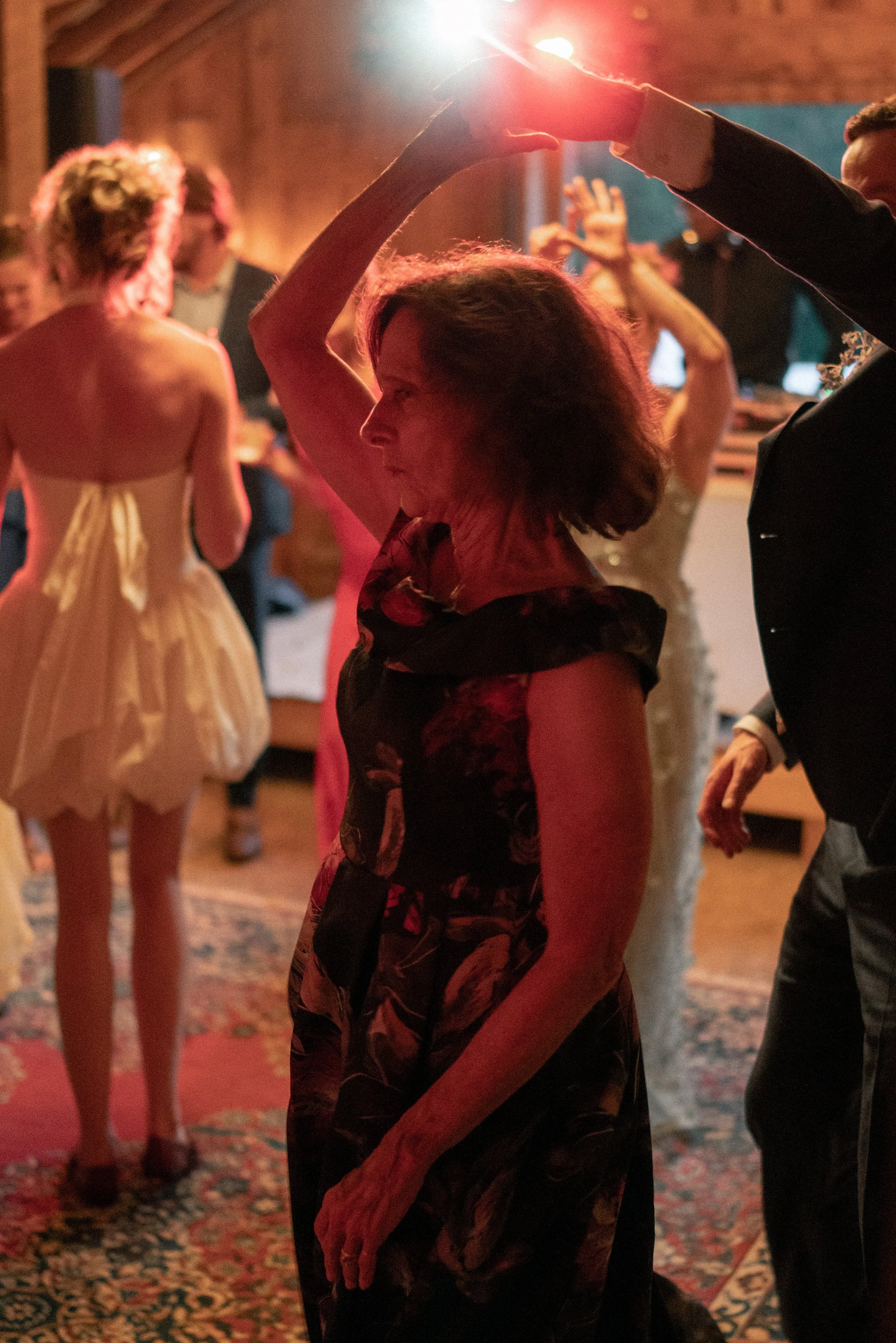People dancing and socializing at a party with warm lighting, a patterned rug, and a wooden ceiling visible in the background.