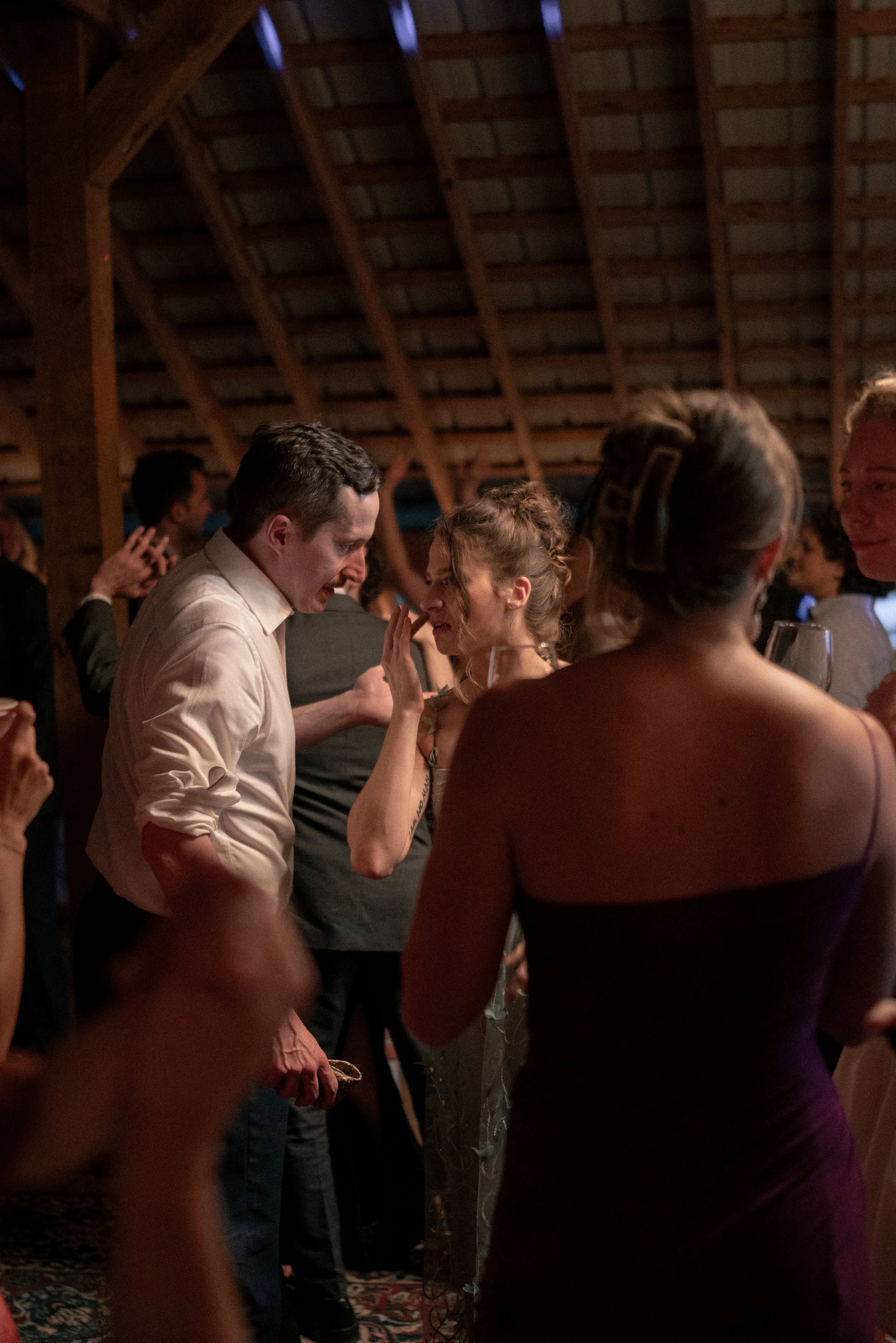 People dancing closely together at a social event in a venue with a wooden ceiling.