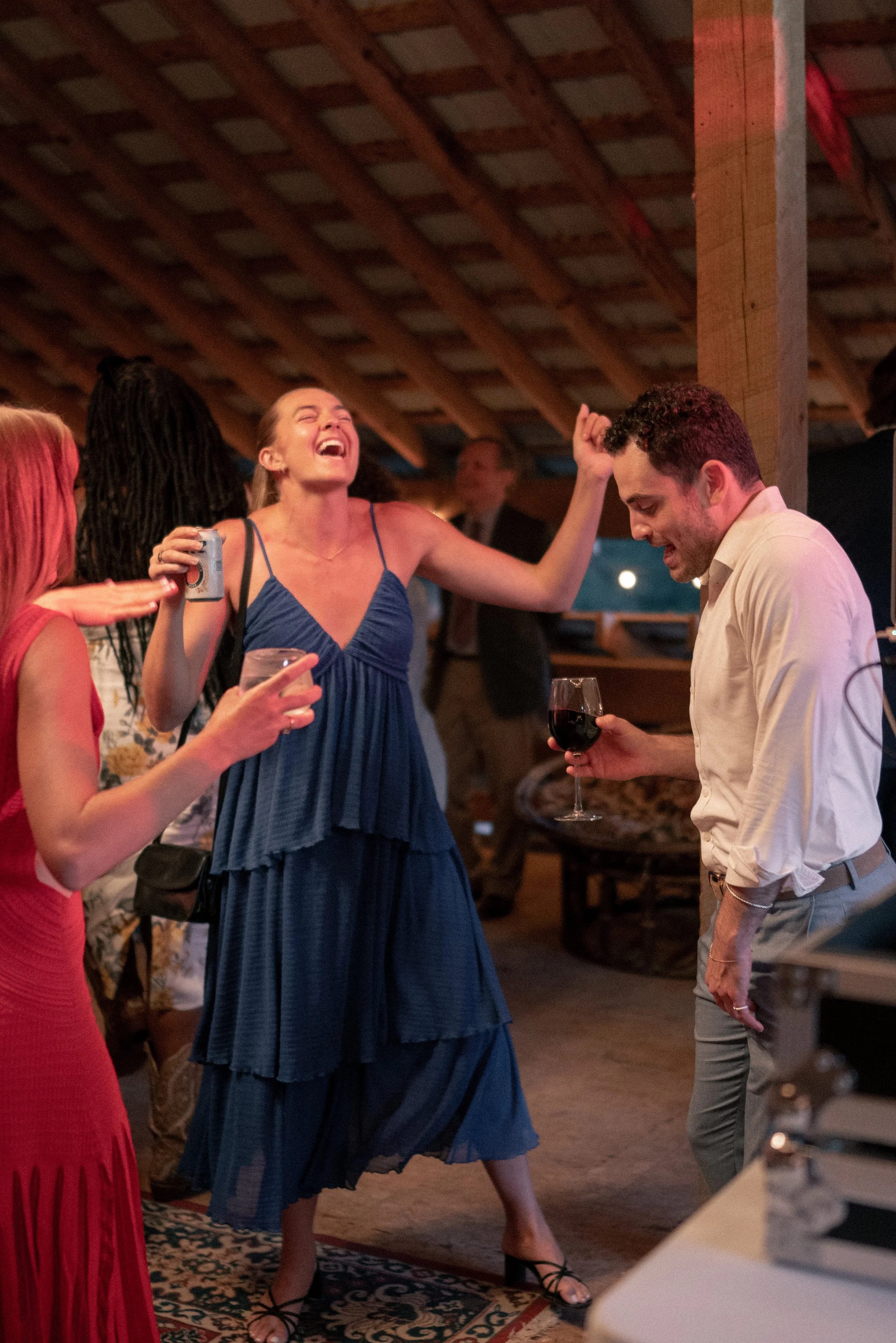 People dancing and socializing at a party in a warmly lit, rustic indoor setting.