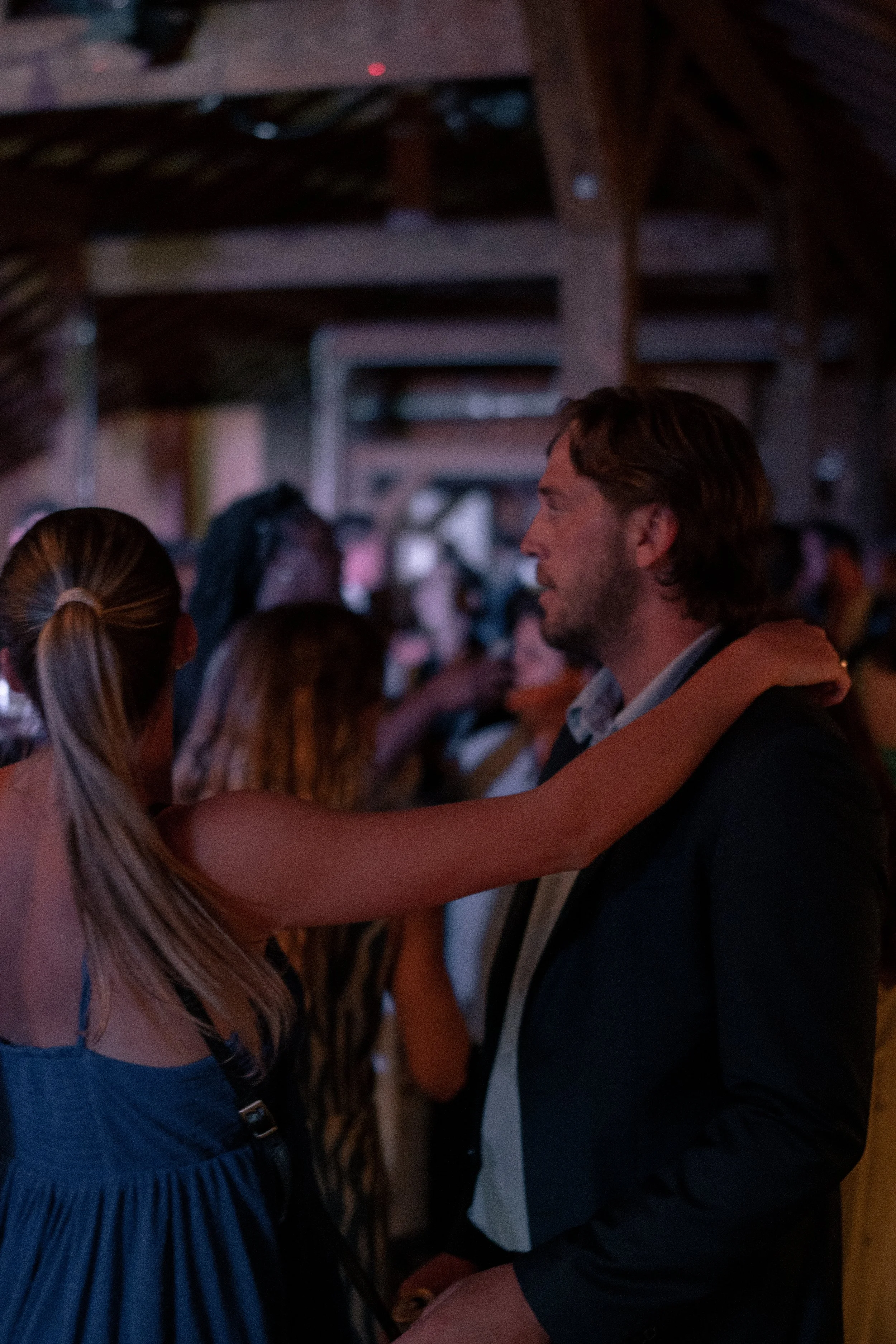 A man with brown hair and a beard dancing closely with a woman with long blonde hair in a crowd at a social event.