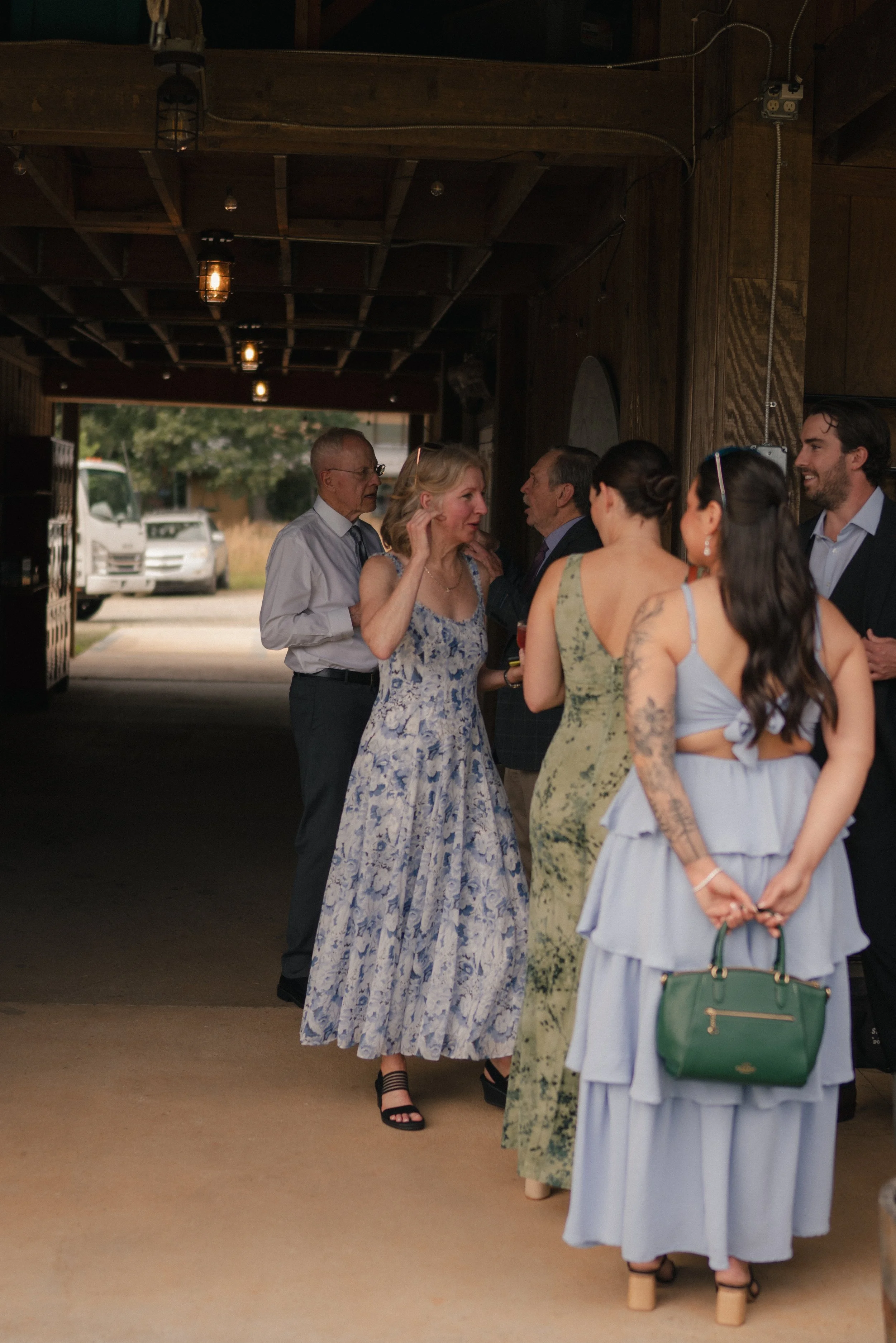 Group of people at a social gathering indoors, dressed in casual summer clothing, talking and smiling.