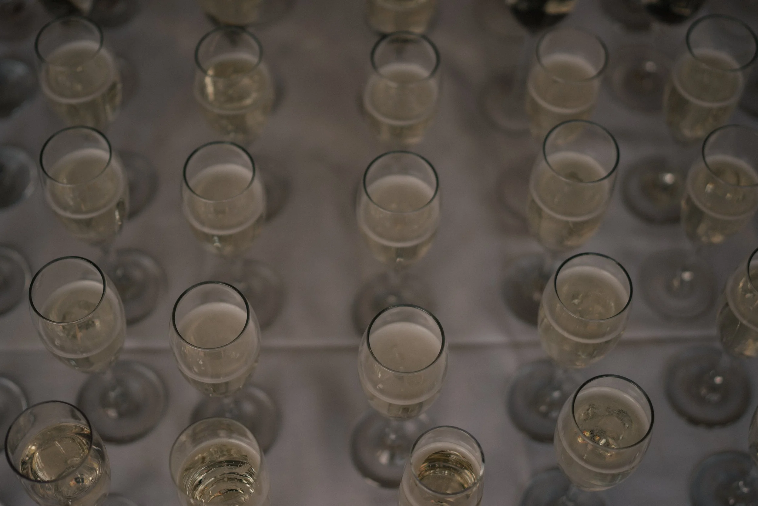 Top-down view of numerous empty champagne glasses arranged in rows on a reflective surface.