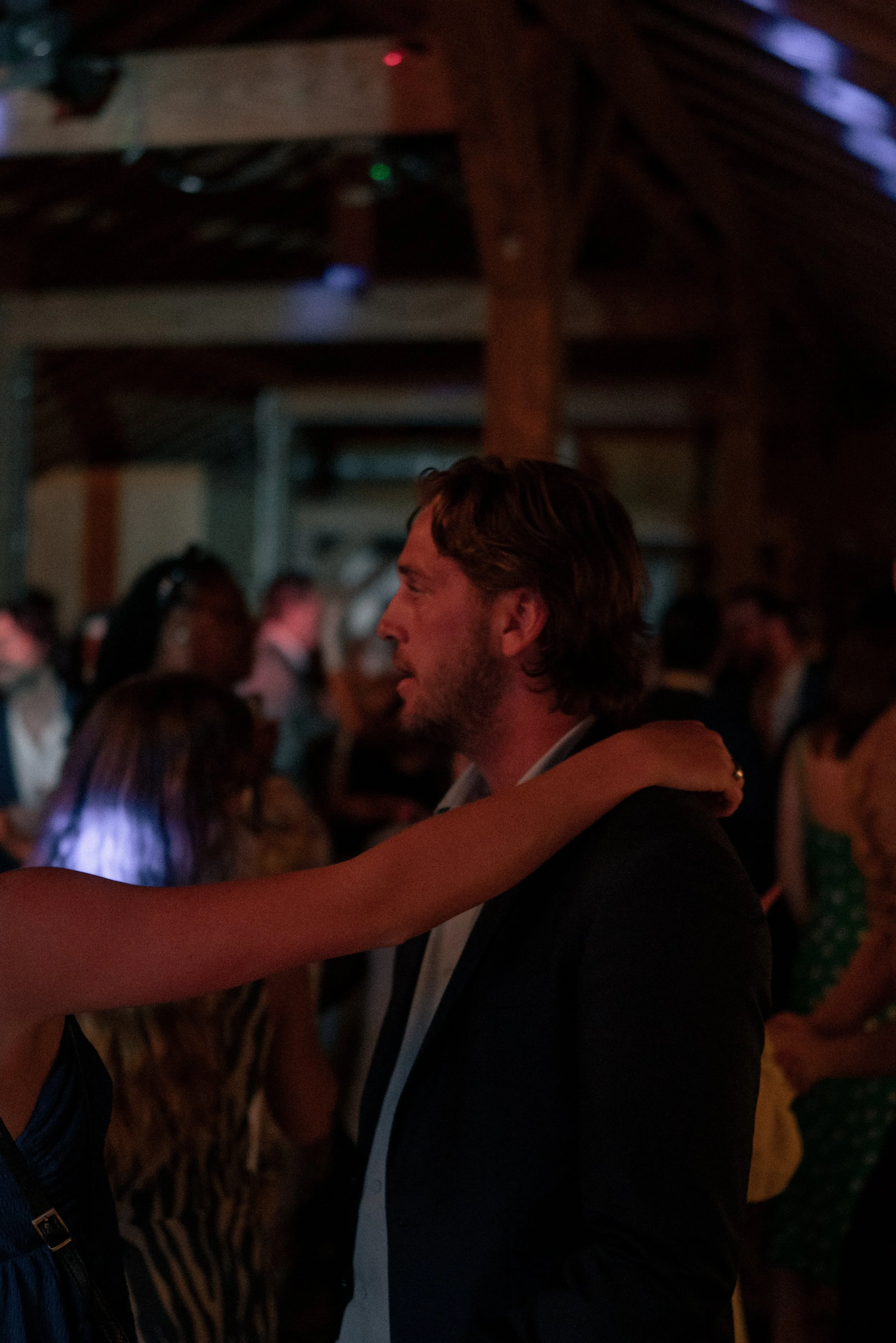 A man and woman embrace at a crowded indoor event in a dimly lit setting.