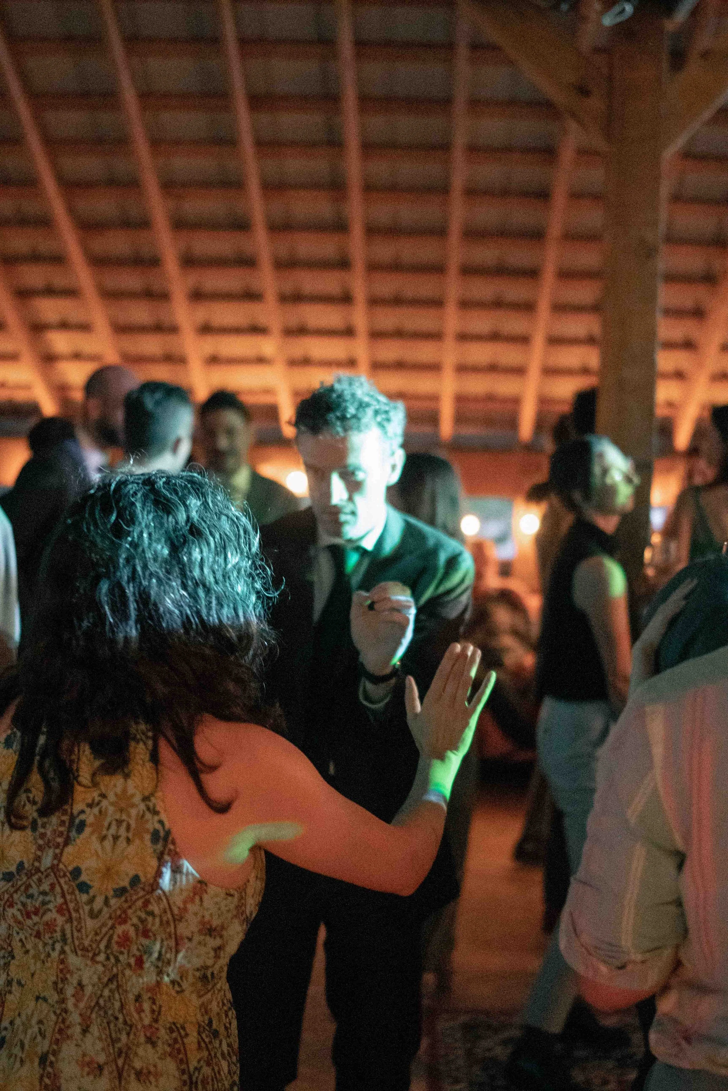 People gathered at an indoor event, socializing and interacting, under warm lighting with a wooden vaulted ceiling in the background.