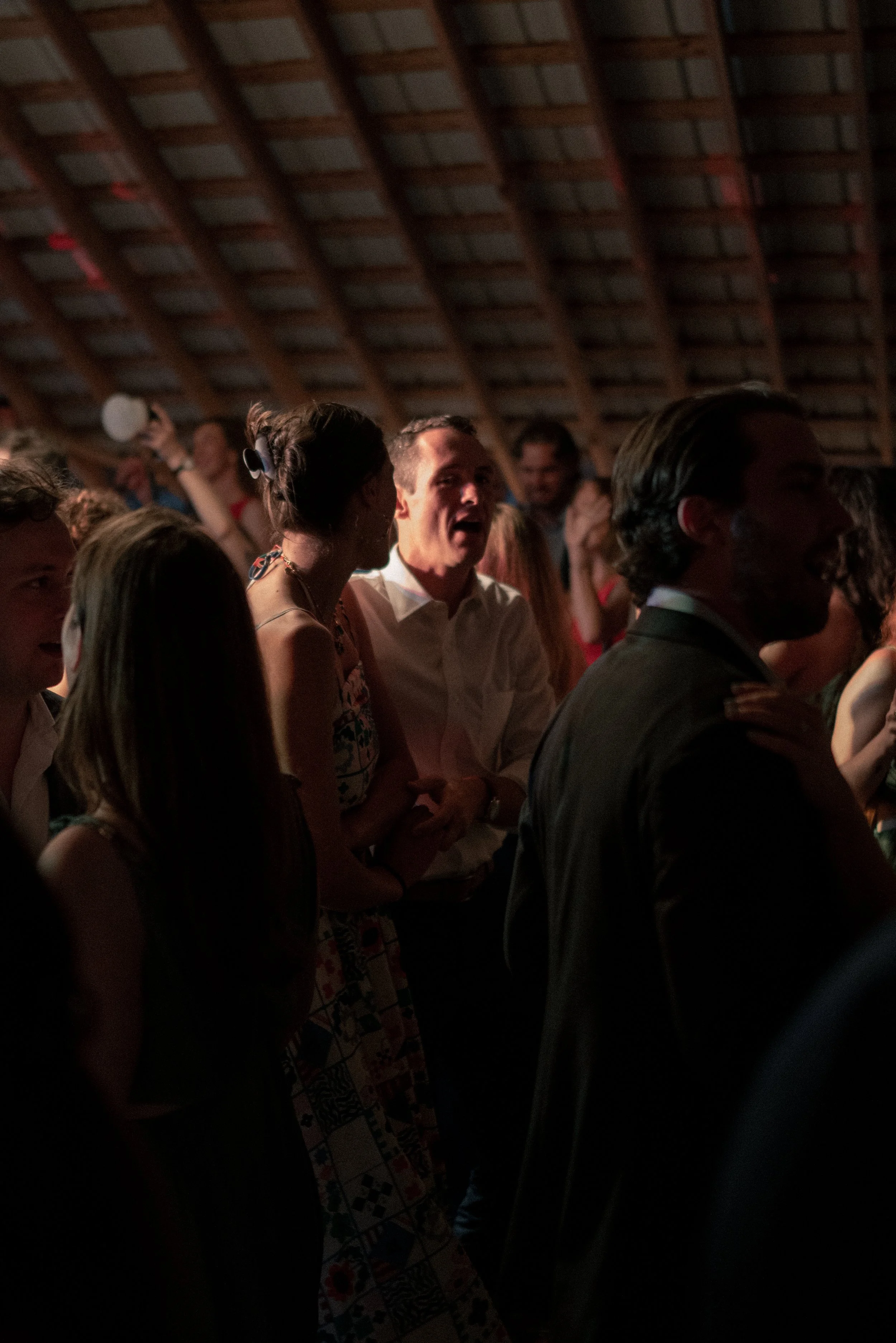 People dancing and socializing at a party or social gathering in a dimly lit venue with wooden roof beams.