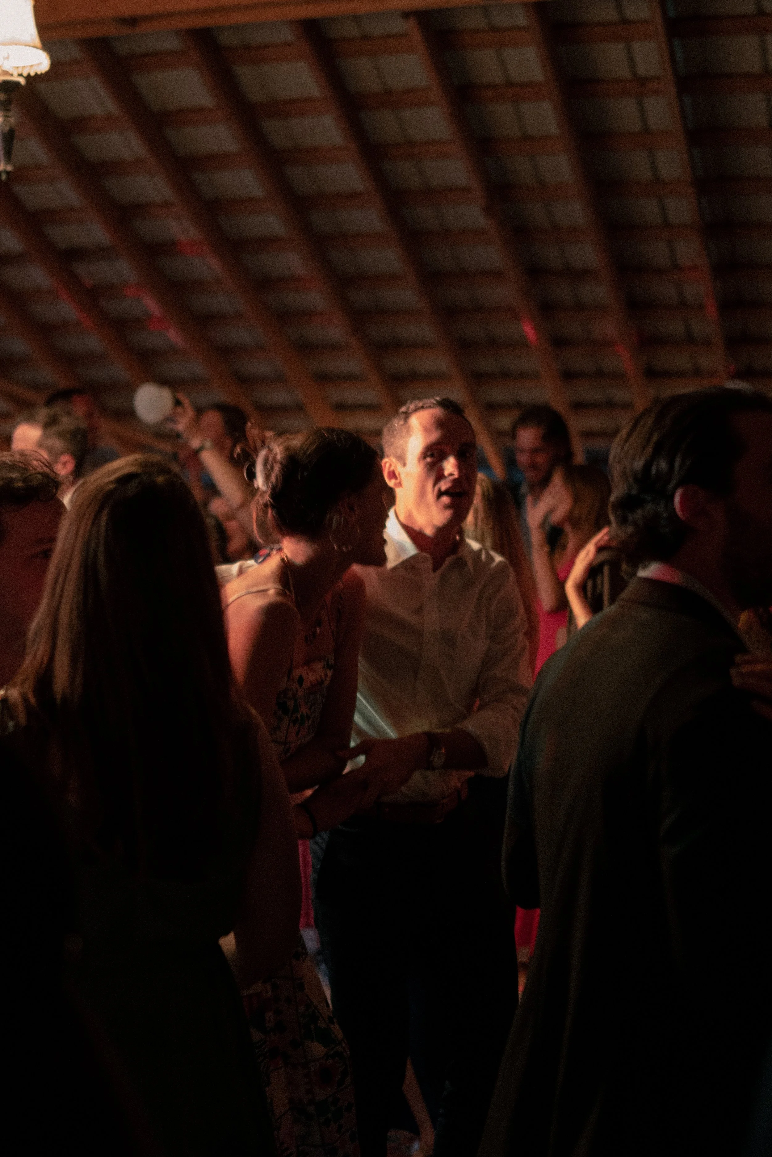 People gathered at an indoor event, engaged in conversation with warm lighting and wooden ceiling beams in the background.