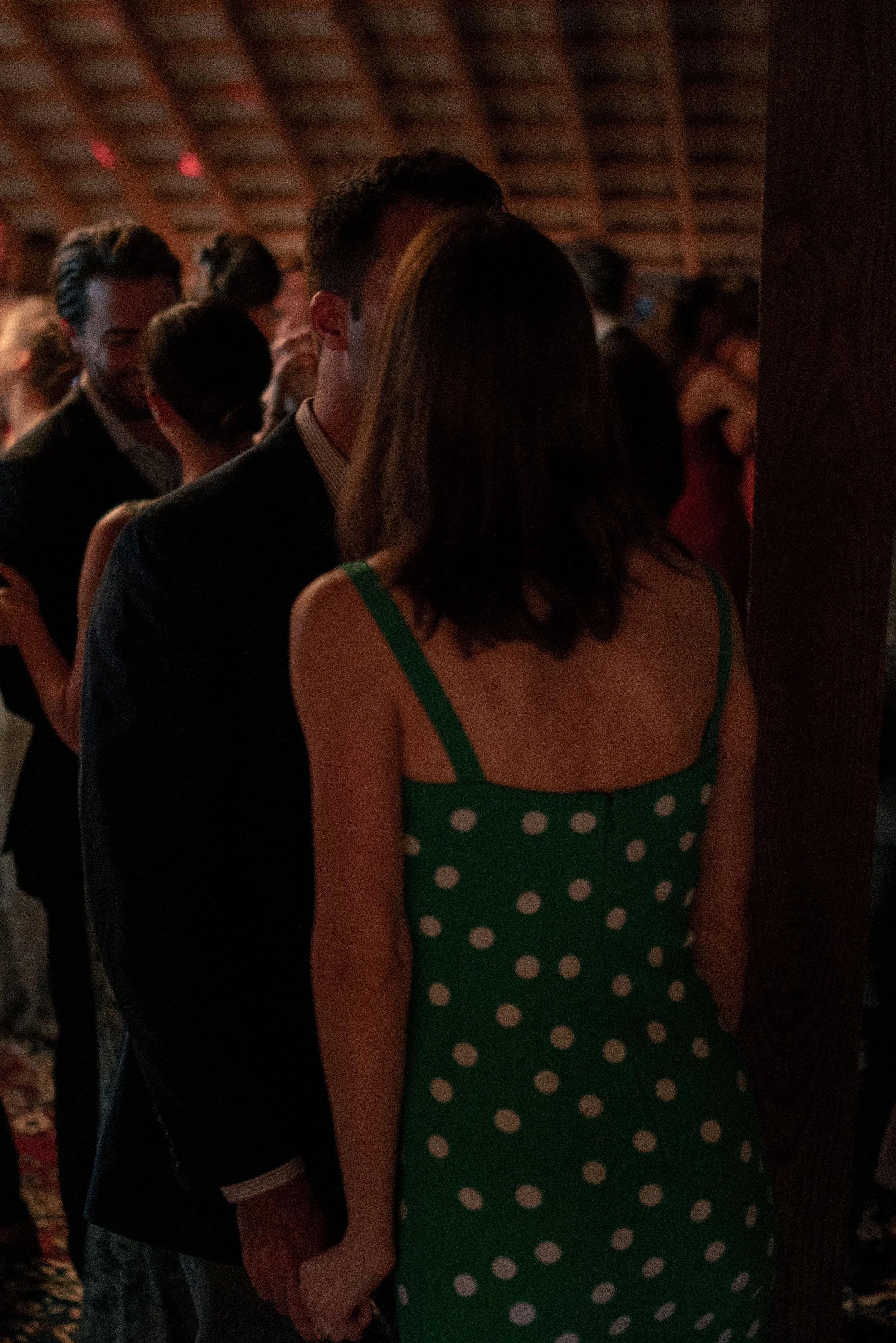 A woman in a green polka dot dress holding hands with an older man in a suit at a social event.