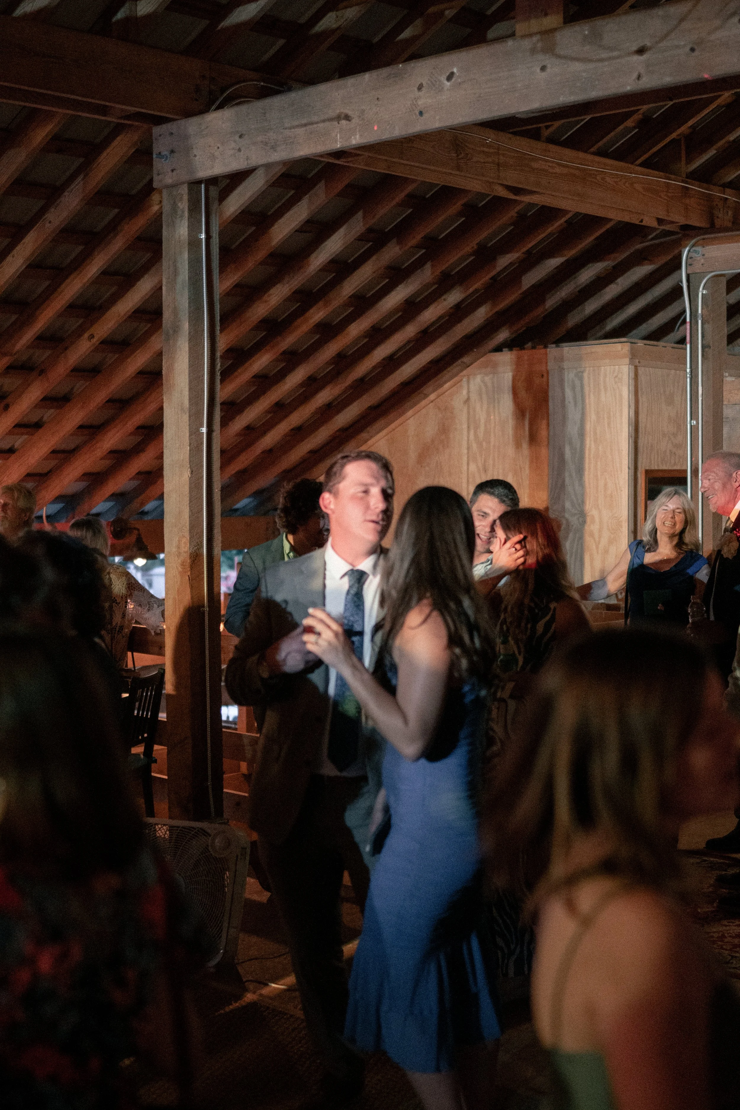 People dancing and socializing inside a rustic wooden venue with exposed beams and a wood-paneled interior, during an evening event.
