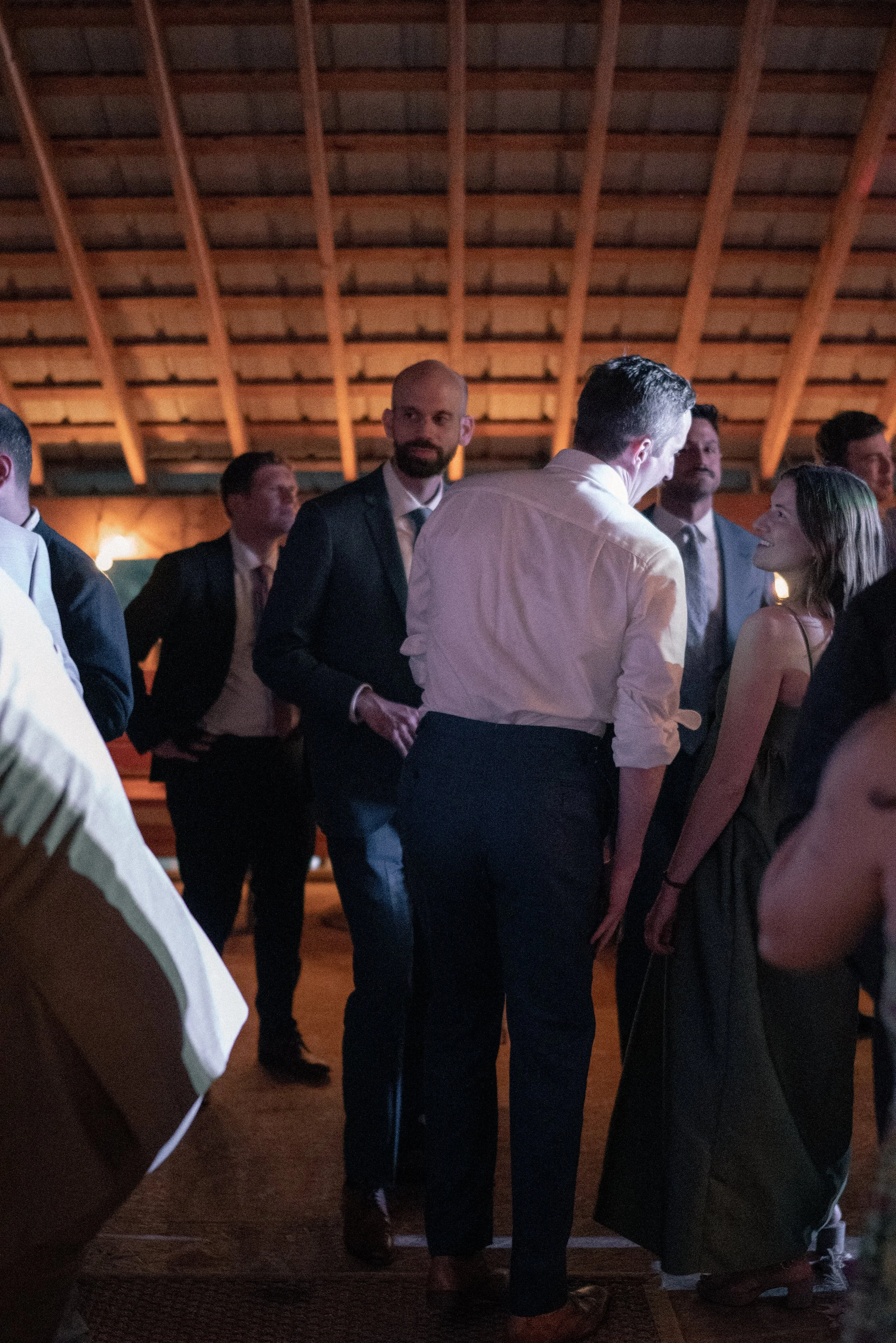 Group of formal-dressed people socializing inside a wooden-paneled building with warm lighting.